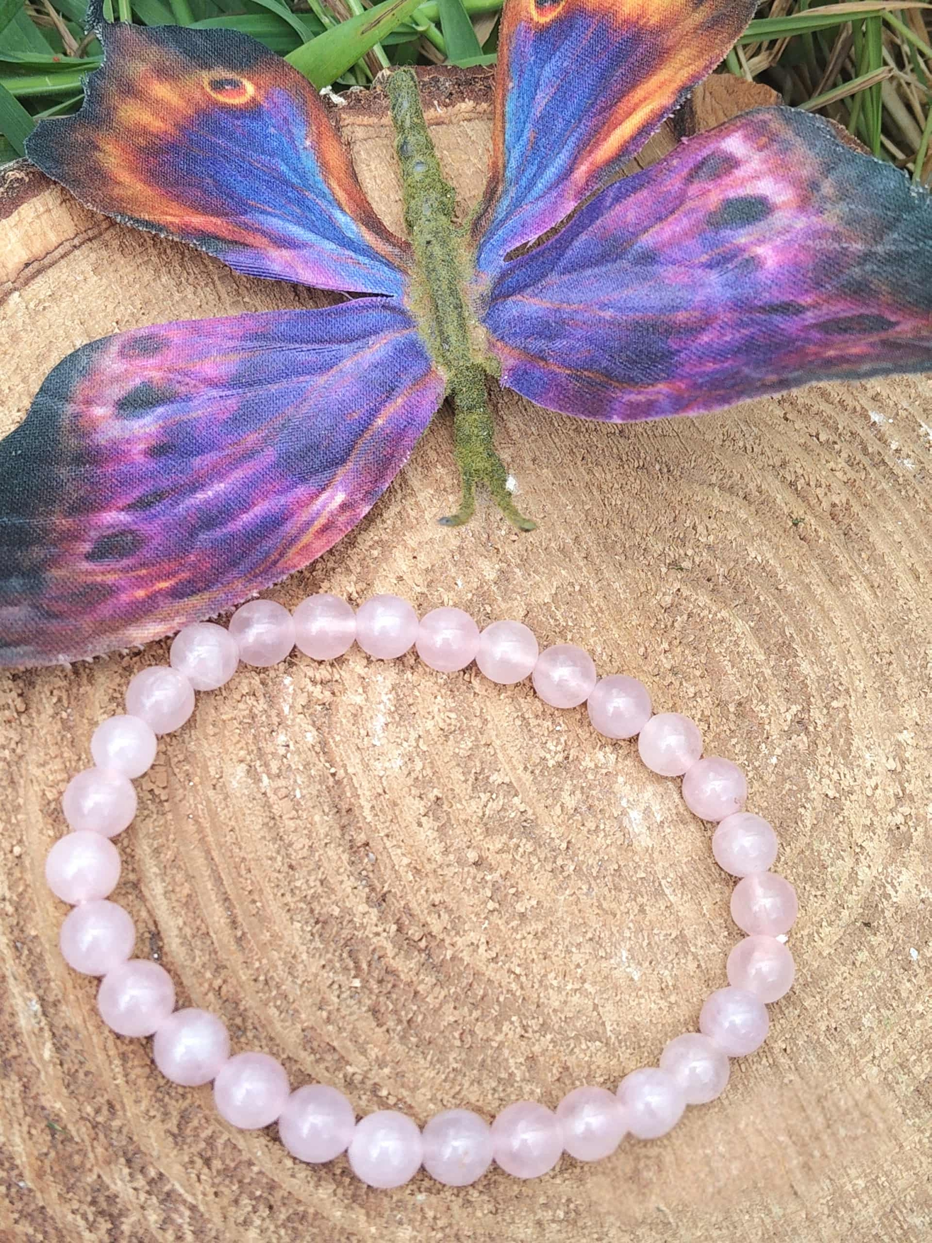 Bracelet quartz rose sur rondin de bois devant papillon violet, amour de soi, douceur du lien et stabilité émotionnelle