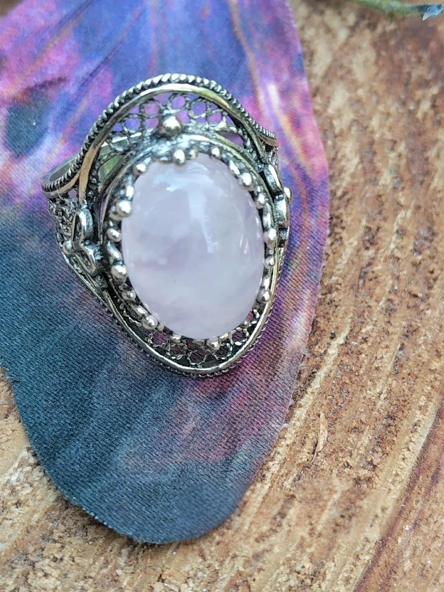 Bague quartz rose en cabochon sur monture filigrane argent 925, posée sur bois avec papillon en tissu en décor, lumière douce révélant son éclat laiteux, symbole d’apaisement, de tendresse et d’équilibre émotionnel