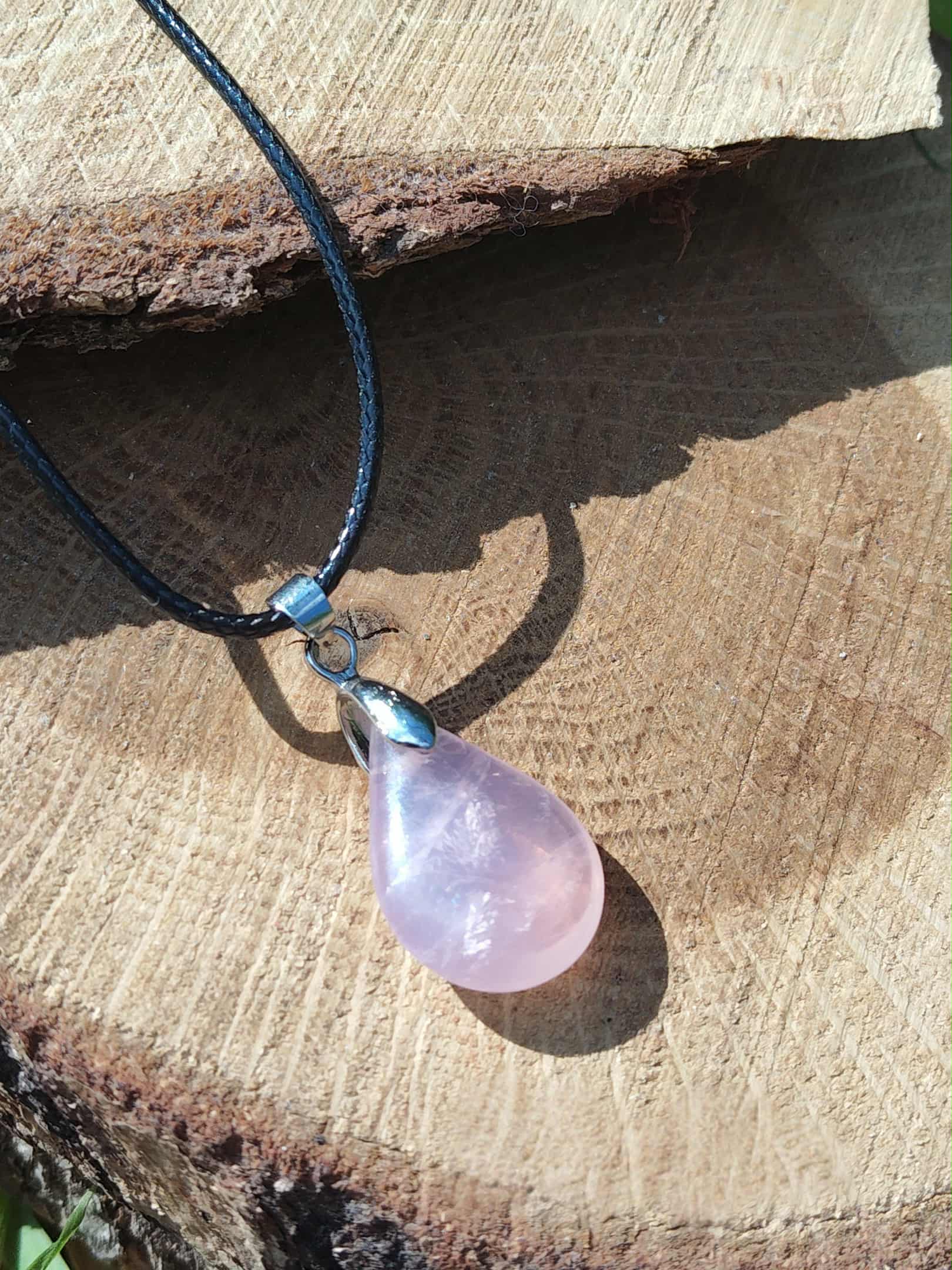 Pendentif goutte en quartz rose sur bois en lumière naturelle, collier pierre naturelle associé au réconfort, au calme des pensées et à l’apaisement émotionnel.