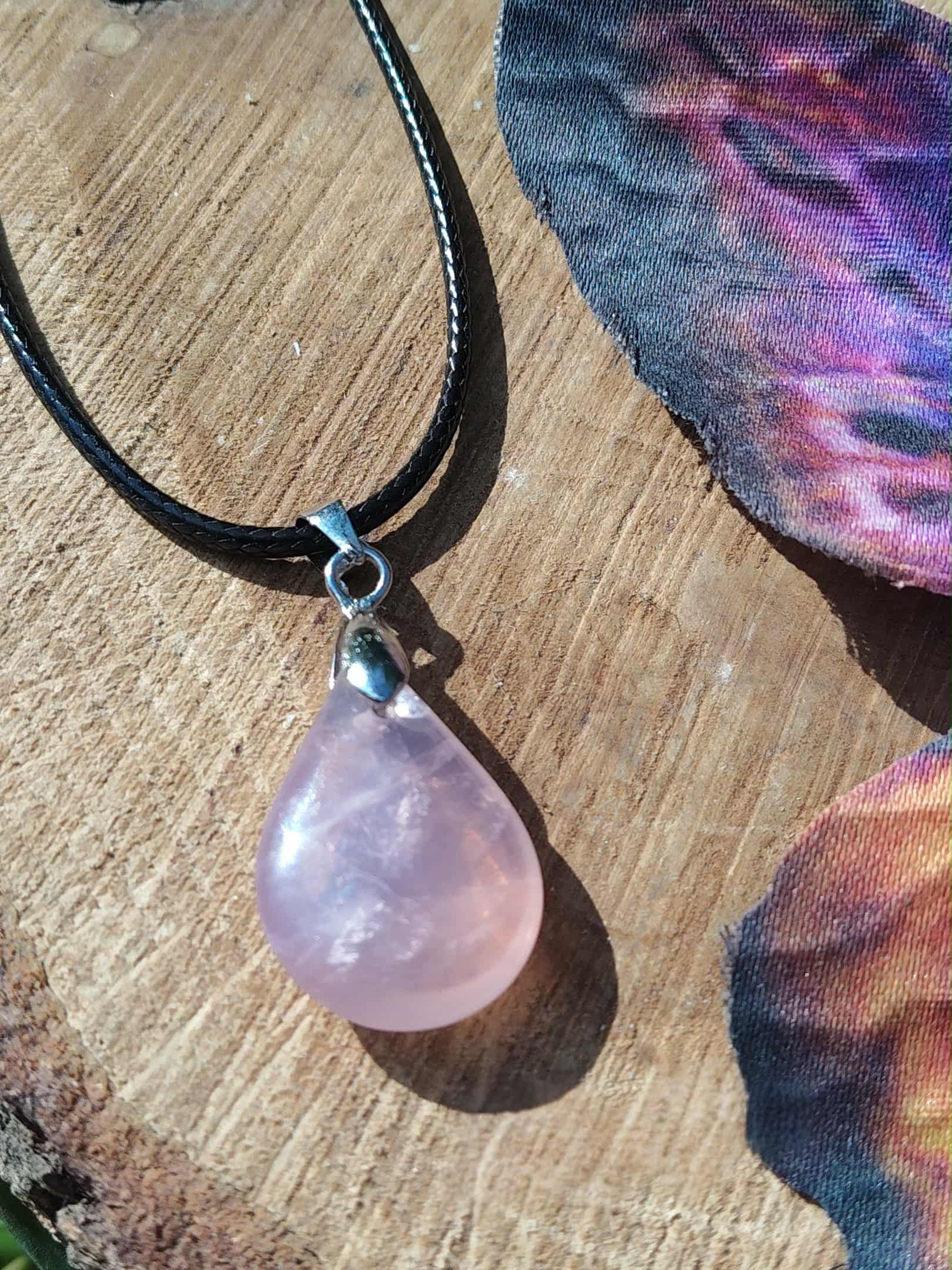Pendentif goutte en quartz rose sur cordon noir, présenté sur tranche de bois, bijou naturel lié à la sérénité, à l’écoute de soi et à la douceur du cœur.