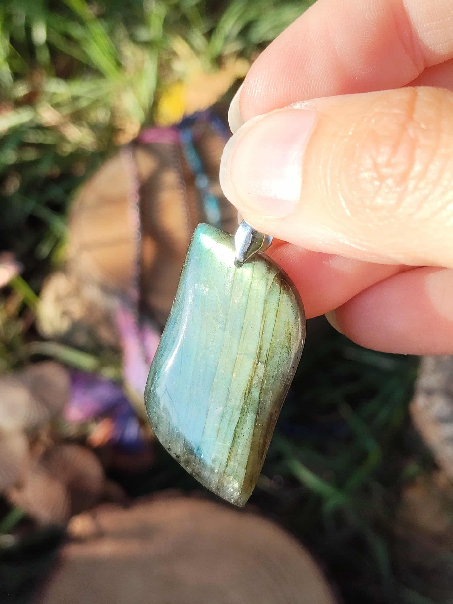 Pendentif labradorite verte tenu en main, reflets bleu-vert, décor galets – protection