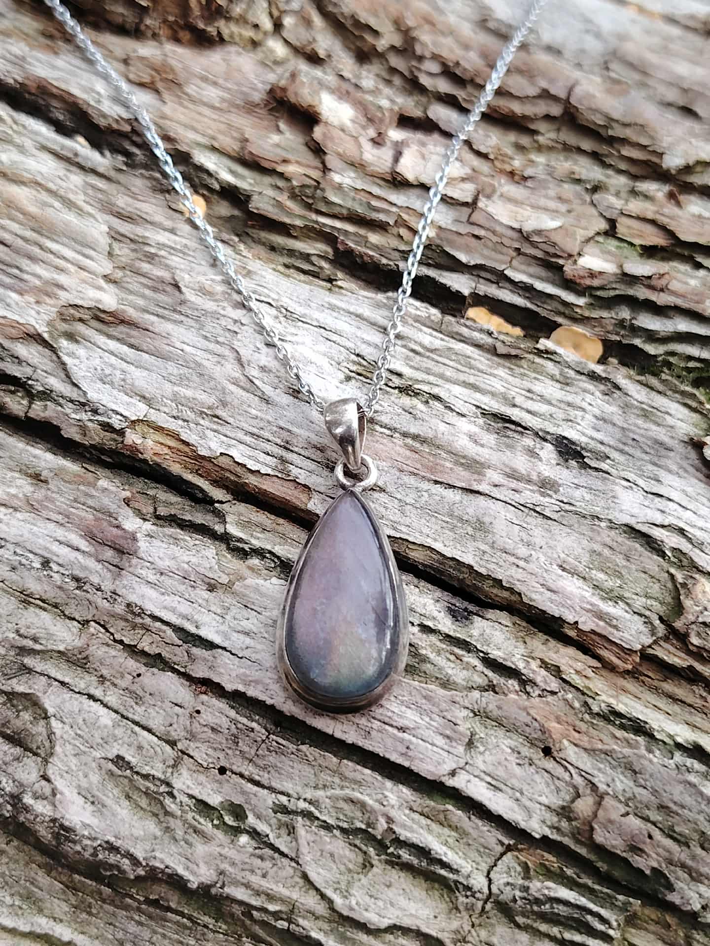 Collier labradorite violette posé sur tronc texturé en ambiance forêt et rivière, bijou en pierre naturelle associé à l’ancrage doux, à la protection et à la clarté.