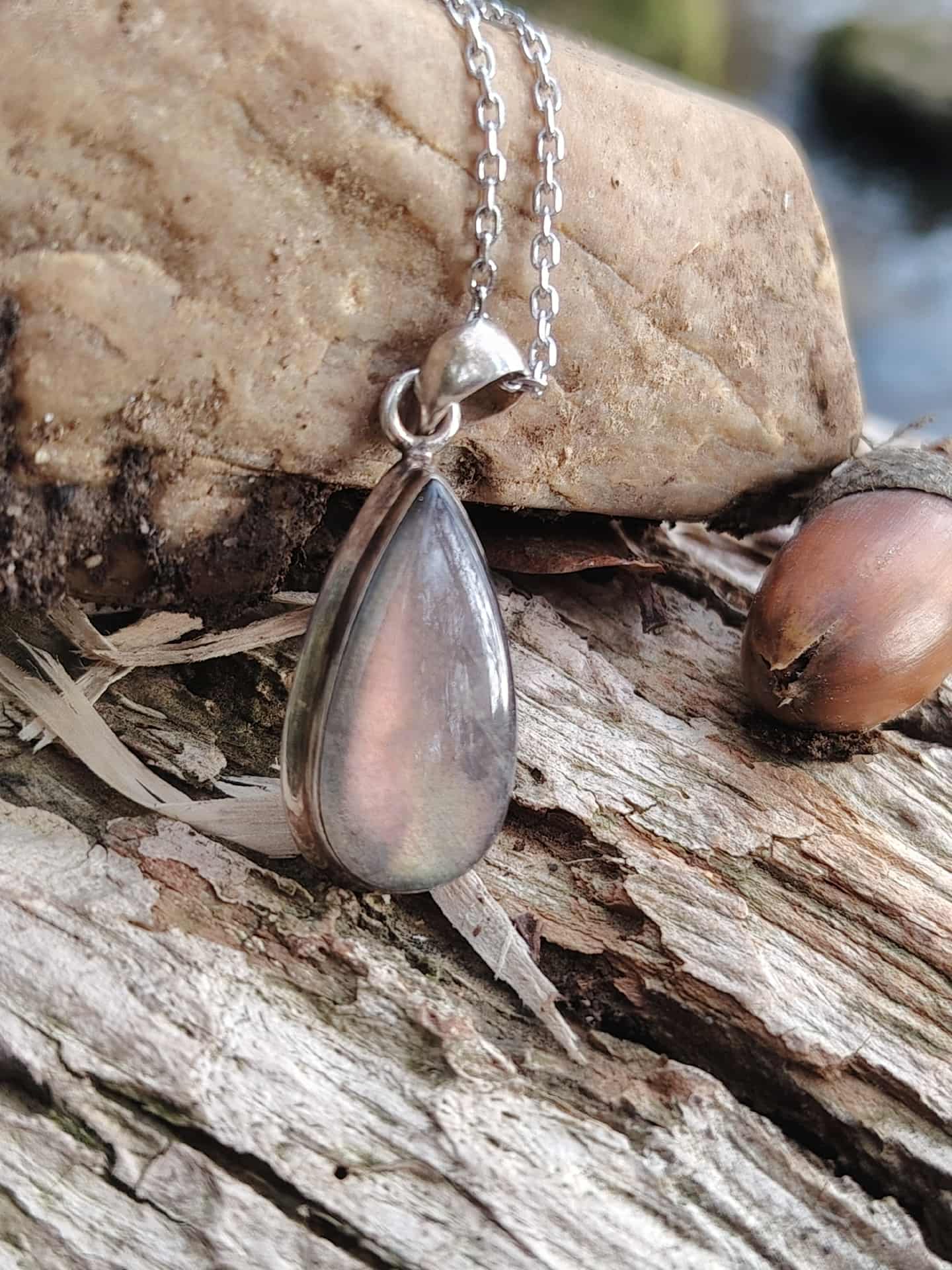 Pendentif labradorite violette sur bois texturé en ambiance bord d’eau, bijou en argent 925 associé à la lucidité, à la protection subtile et au recentrage.