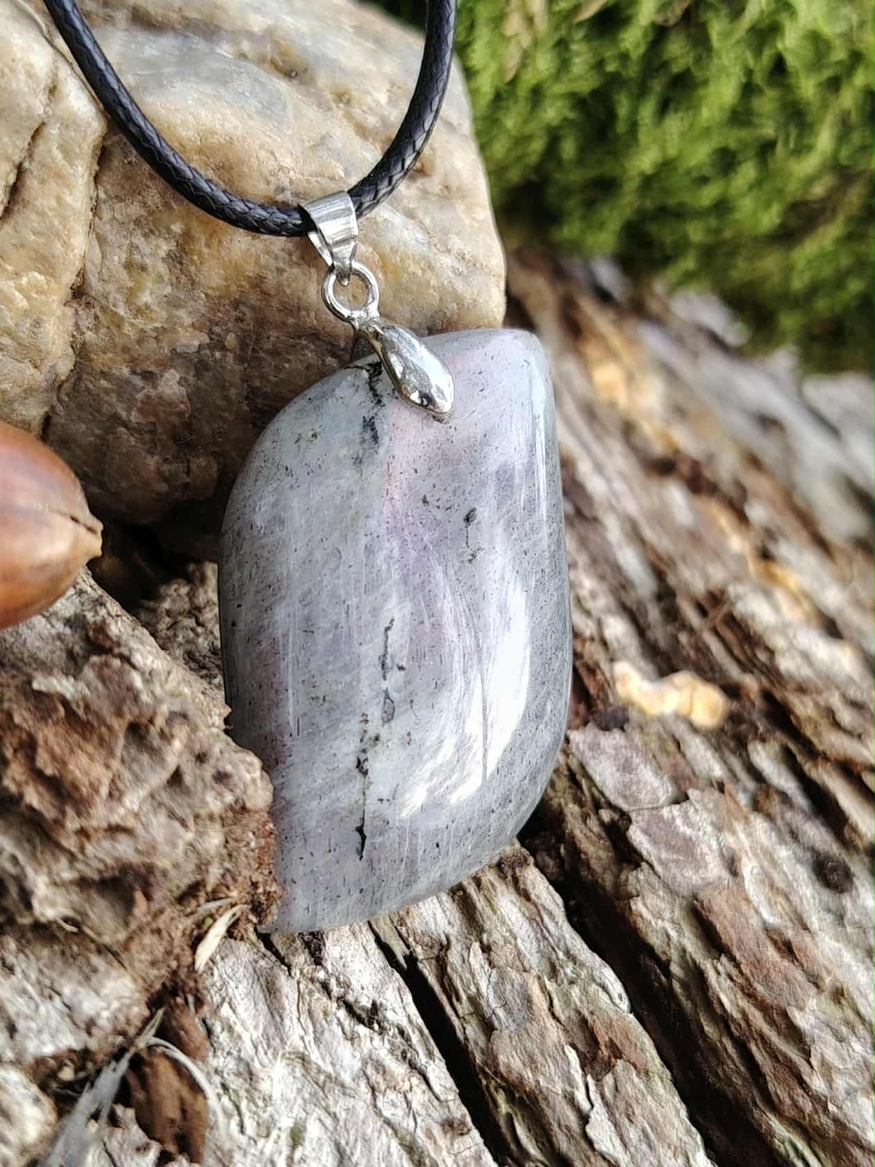 Pendentif labradorite grise aux reflets arc-en-ciel sur cordon noir, posé sur bois et roche, bijou en pierre naturelle associé à la protection douce, à l’ancrage et à l’intuition.