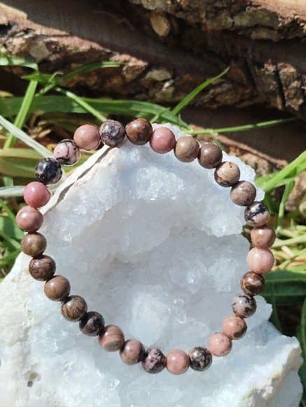 Bracelet rhodonite 6 mm présenté sur pierre claire avec herbes naturelles, écoute de soi, paix affective et équilibre intérieur