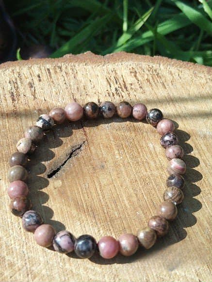 Bracelet rhodonite 6 mm sur support en bois avec feuillage vert, pardon intérieur, apaisement affectif et émotions plus douces
