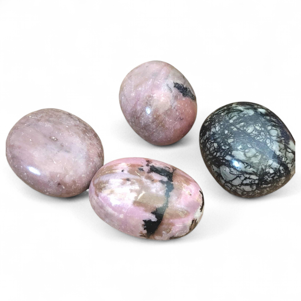 Quatre pierres roulées rhodonite aux teintes roses et noires présentées sur fond blanc, évoquant douceur, apaisement émotionnel et équilibre intérieur.