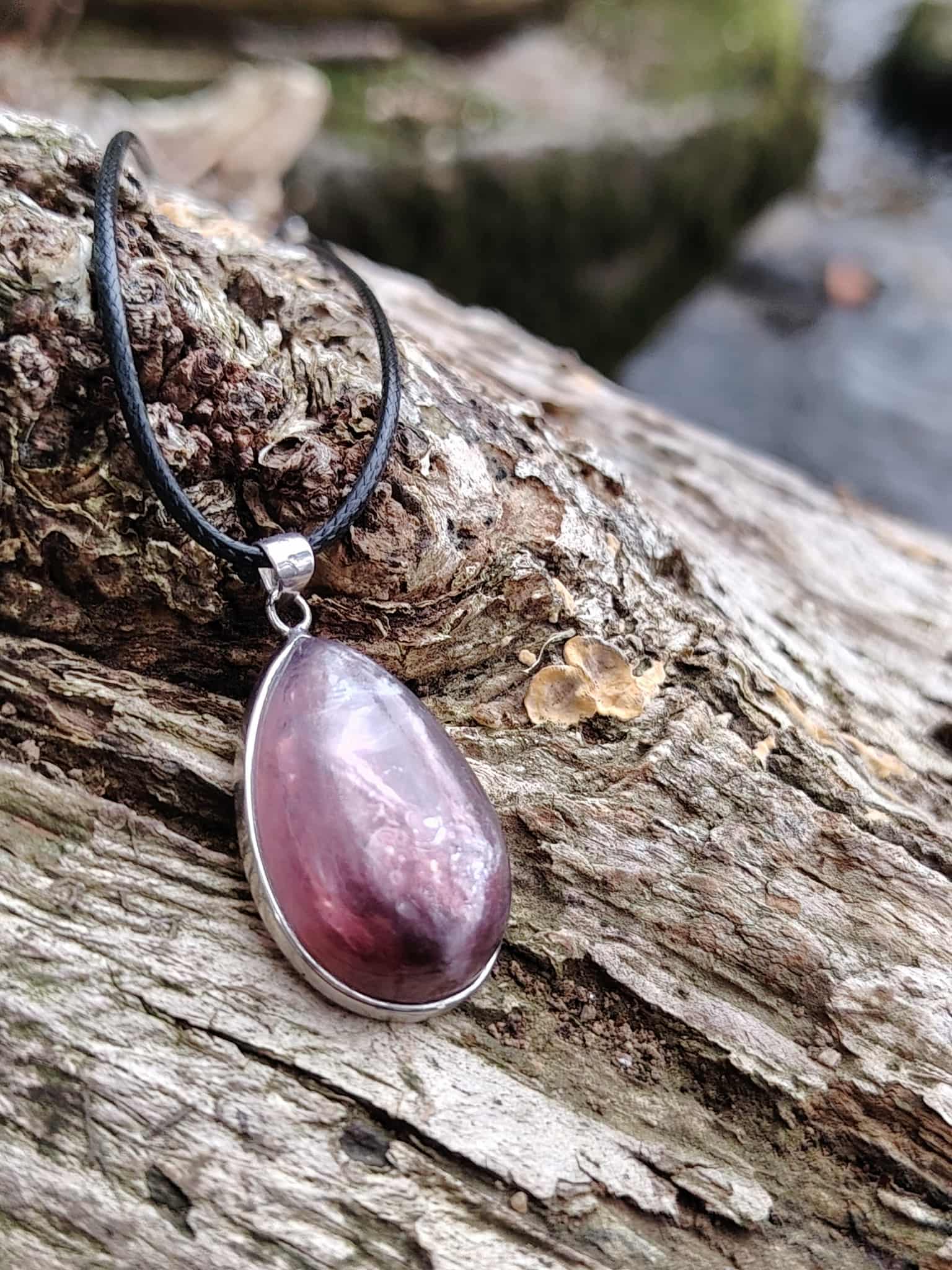 Pendentif lépidolite en argent 925 posé sur bois flotté en bord de mer, bijou en pierre naturelle associé à la sérénité, au lâcher-prise et à l’harmonie émotionnelle.