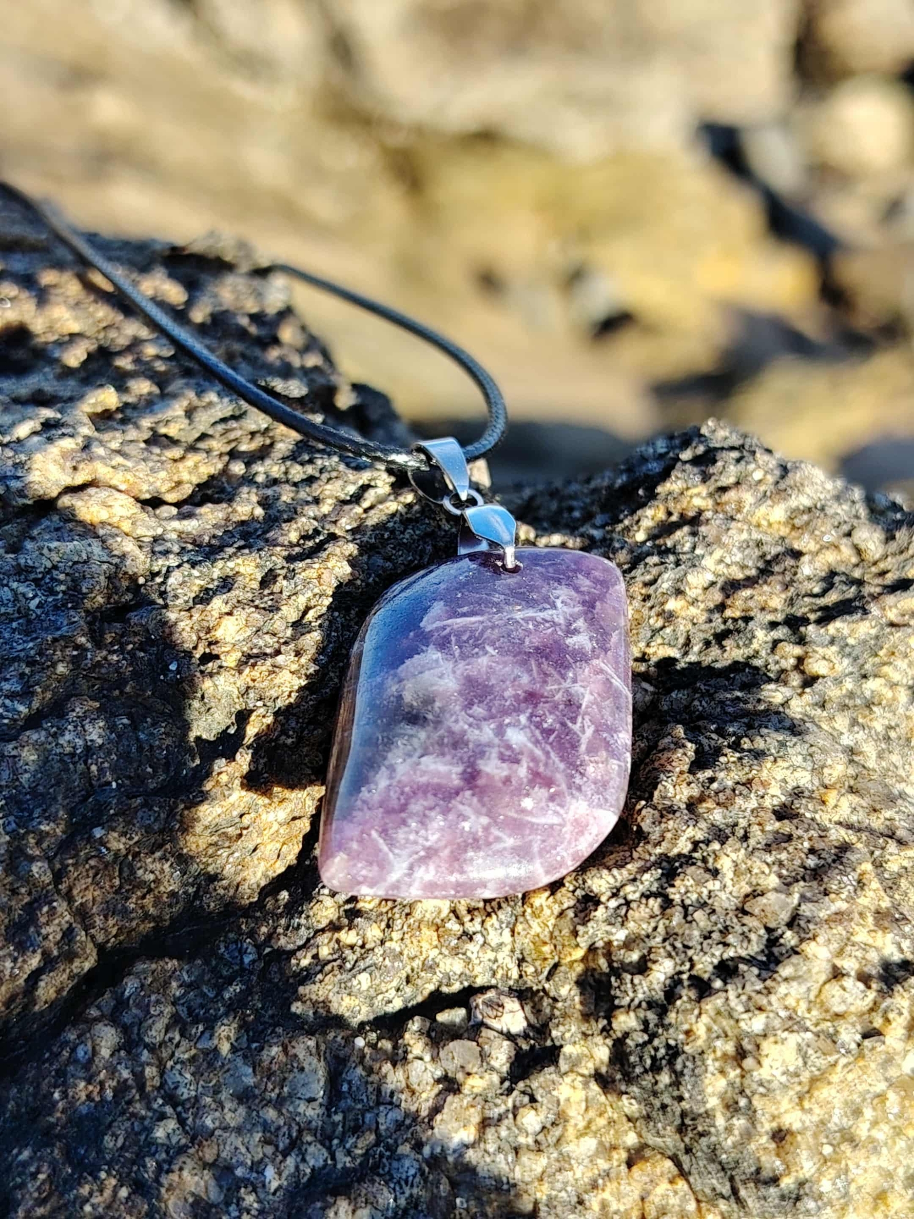 Pendentif lépidolite rectangulaire posé sur rocher en bord de mer en Bretagne, collier pierre naturelle associé à la tranquillité, à l’écoute de soi et à l’harmonie émotionnelle.