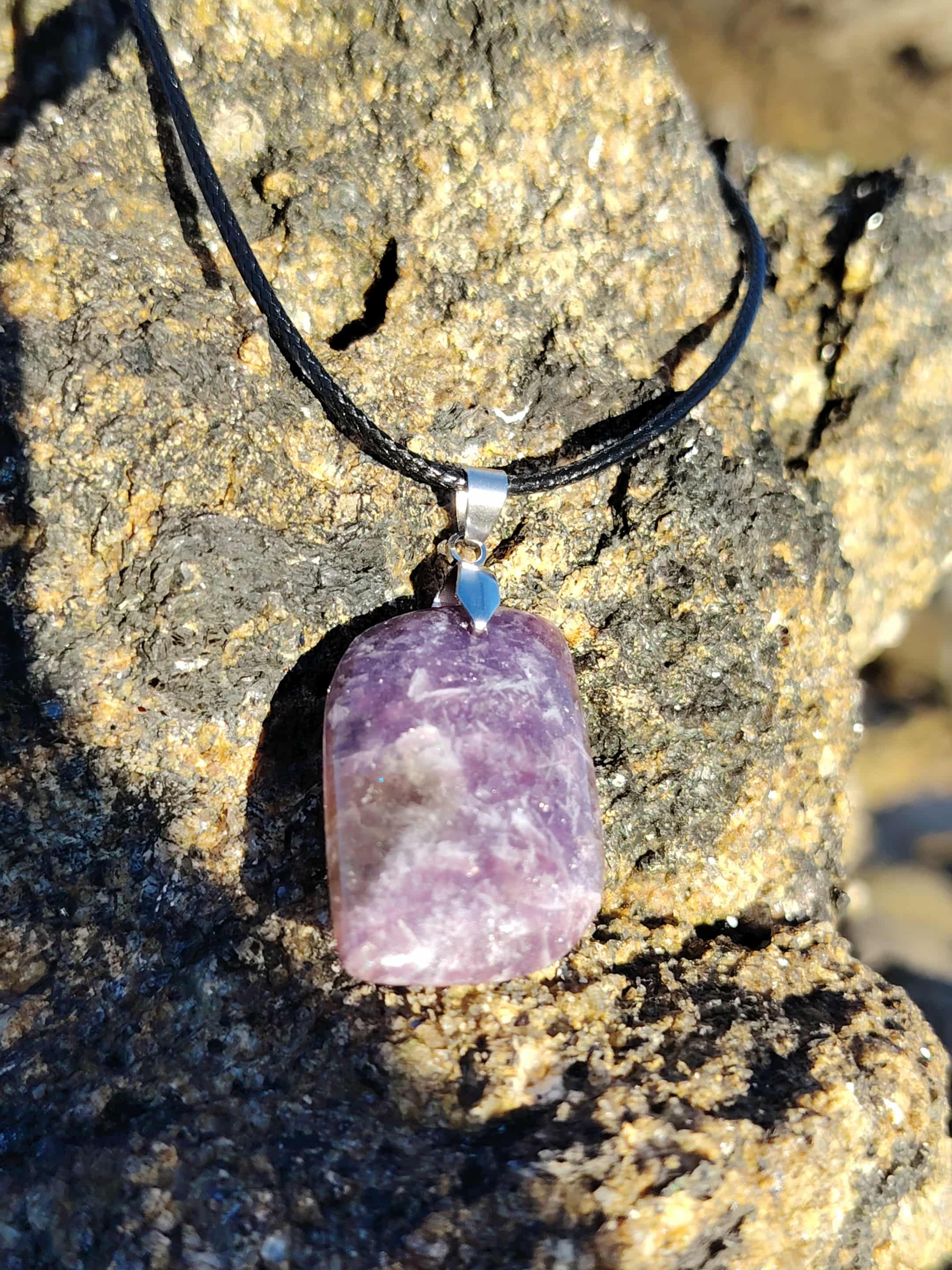 Pendentif lépidolite violette posé sur rocher en bord de mer breton, bijou en pierre naturelle relié aux transitions, au recentrage et à la paix émotionnelle.