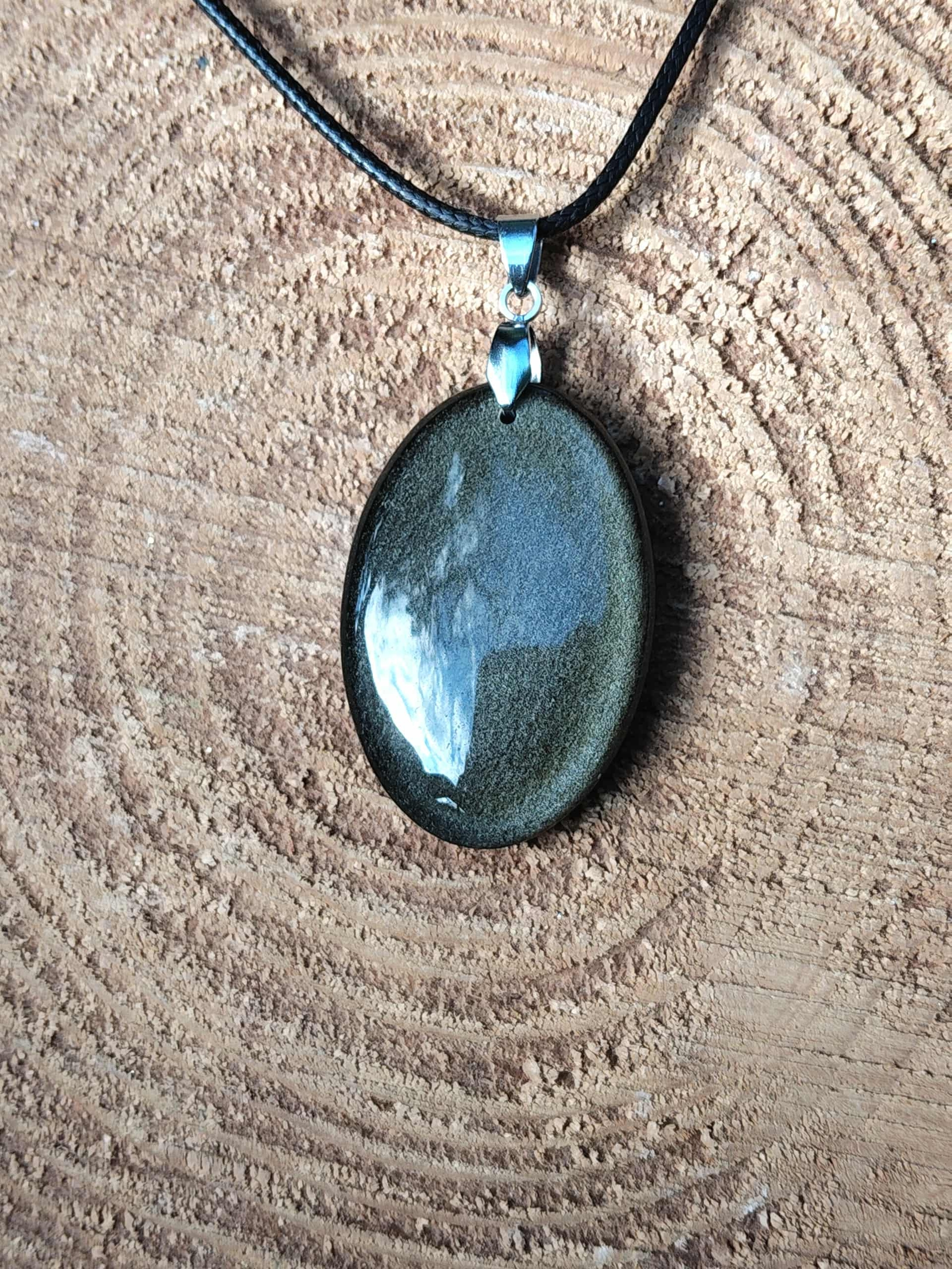 Pendentif obsidienne dorée sur fond bois clair, pierre naturelle évoquant la stabilité, la maîtrise de soi et une énergie plus posée.