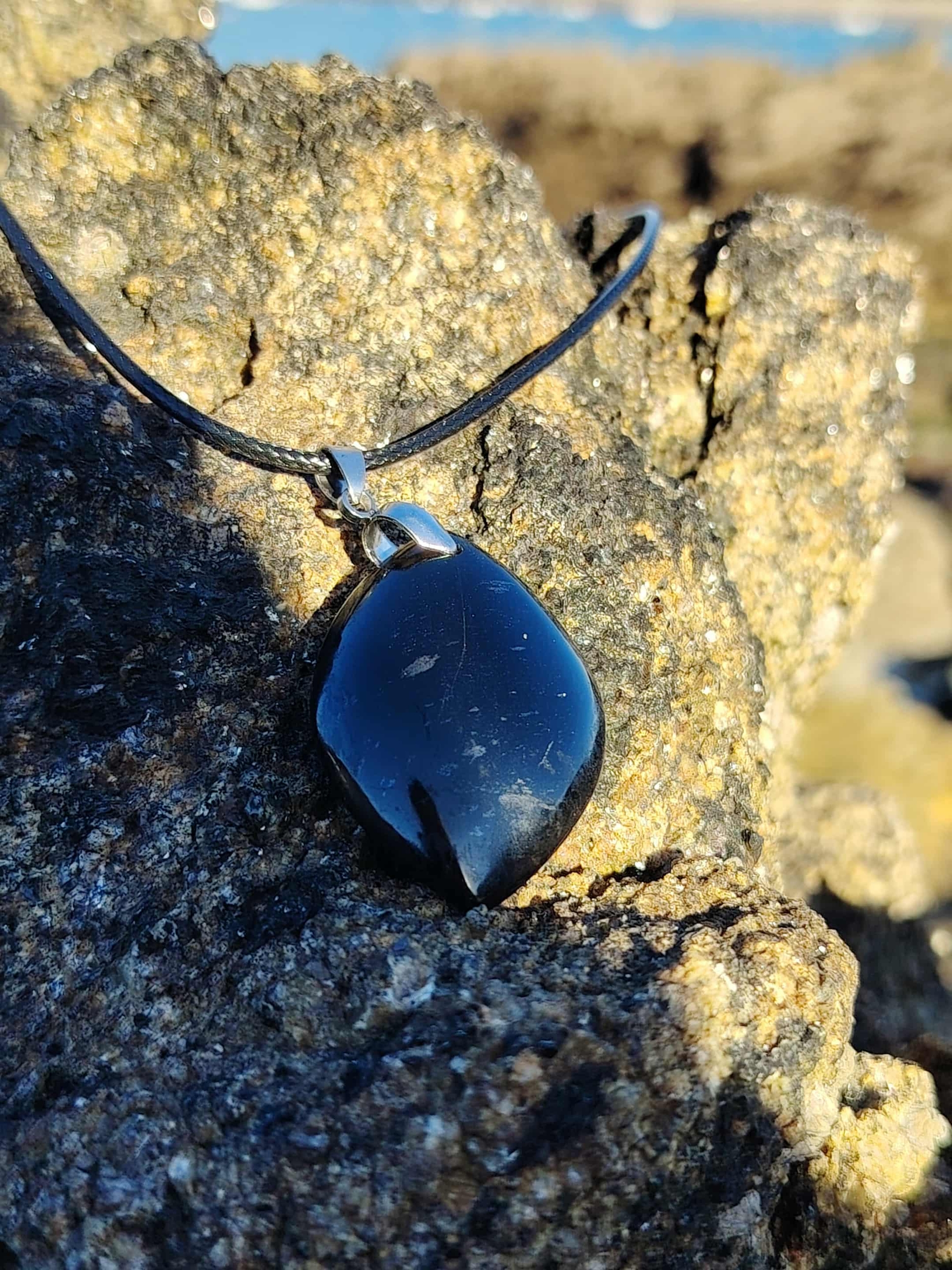 Pendentif tourmaline noire marquise sur rocher en bord de mer en Bretagne, bijou pierre naturelle lié à l’enracinement, à la vigilance et à l’équilibre intérieur.