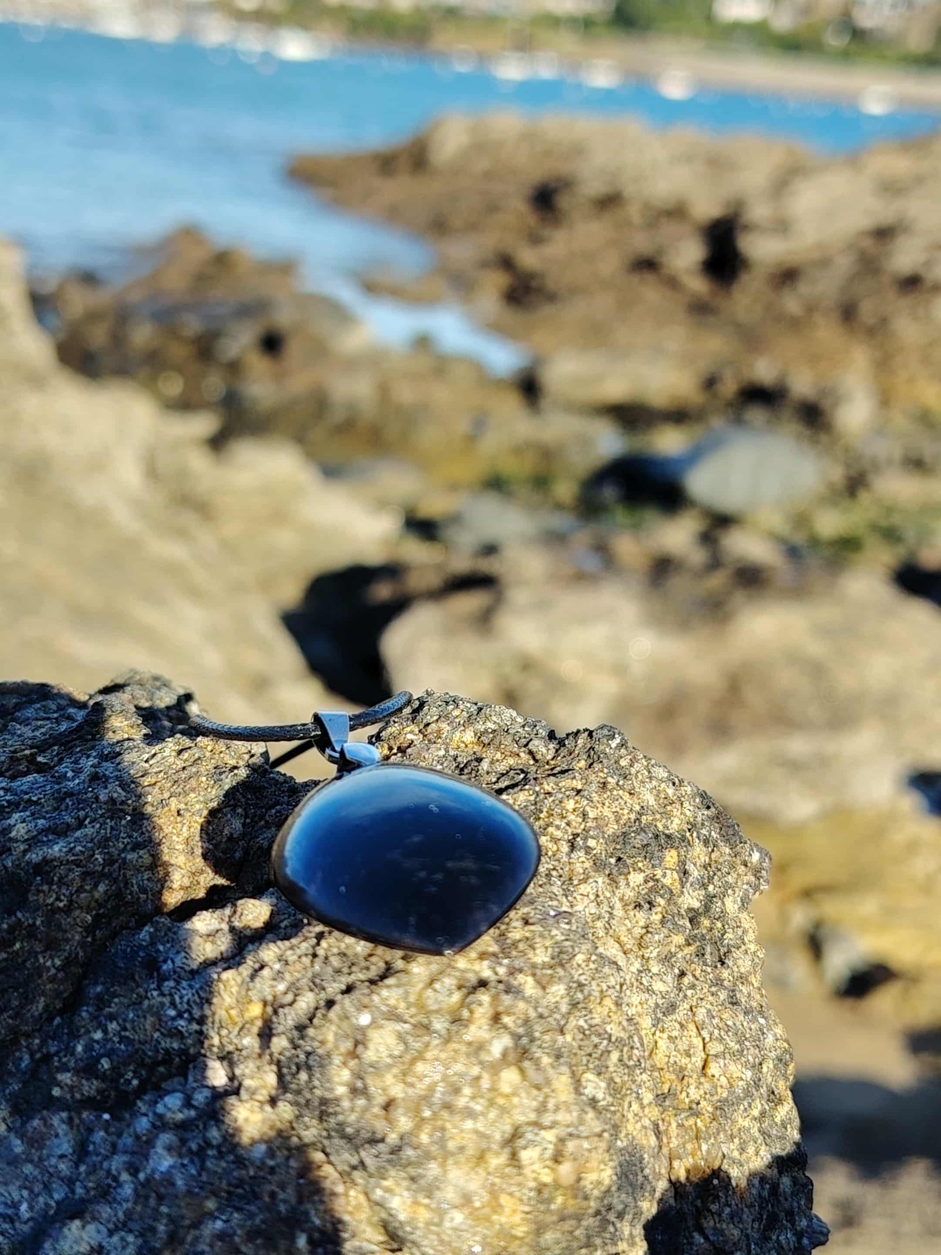 Pendentif tourmaline noire marquise posé sur rocher face à l’océan en Bretagne, pierre naturelle reliée à la protection, à la solidité émotionnelle et au recentrage.