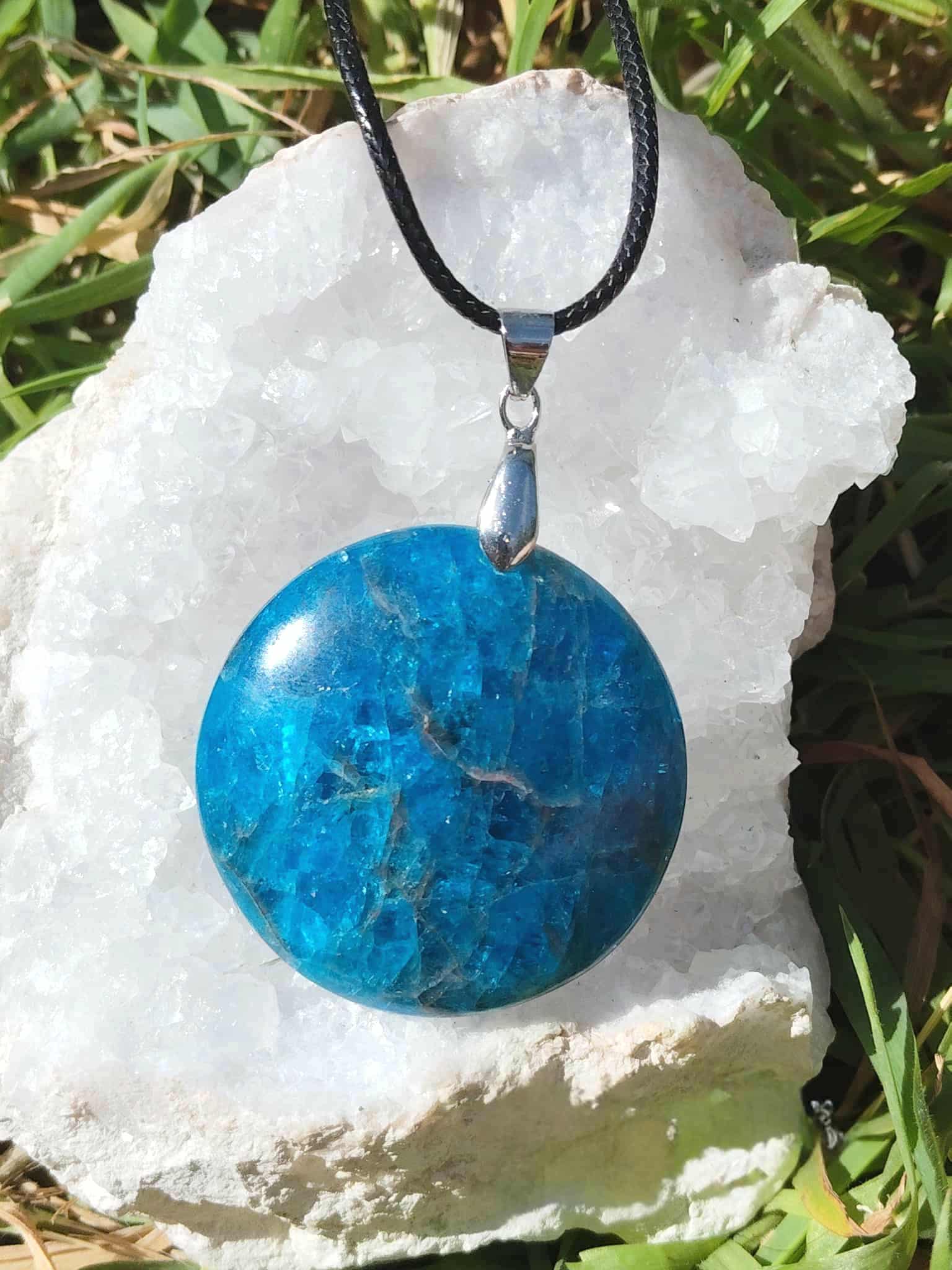 Pendentif apatite bleue ronde sur un amas de quartz  en extérieur, bijou en pierre naturelle associé à la communication, à l’assurance et à l’élan intérieur.