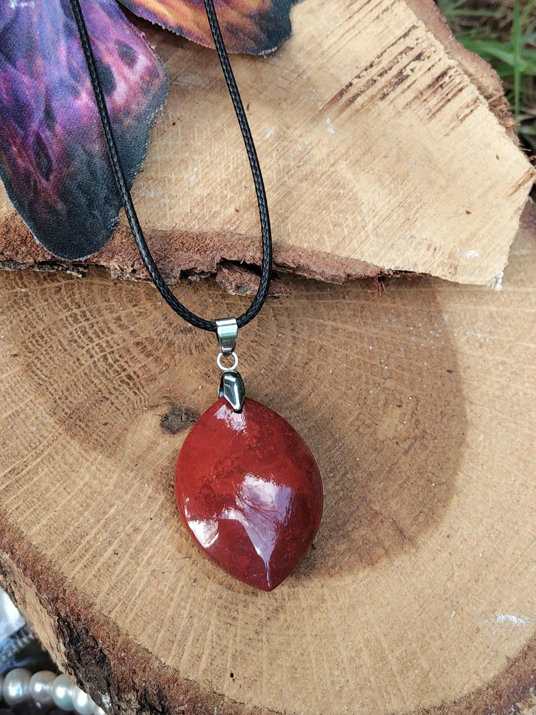 Pendentif jaspe rouge sur rondin de bois, pierre naturelle associée à l’énergie stable, au dynamisme et à l’ancrage profond.