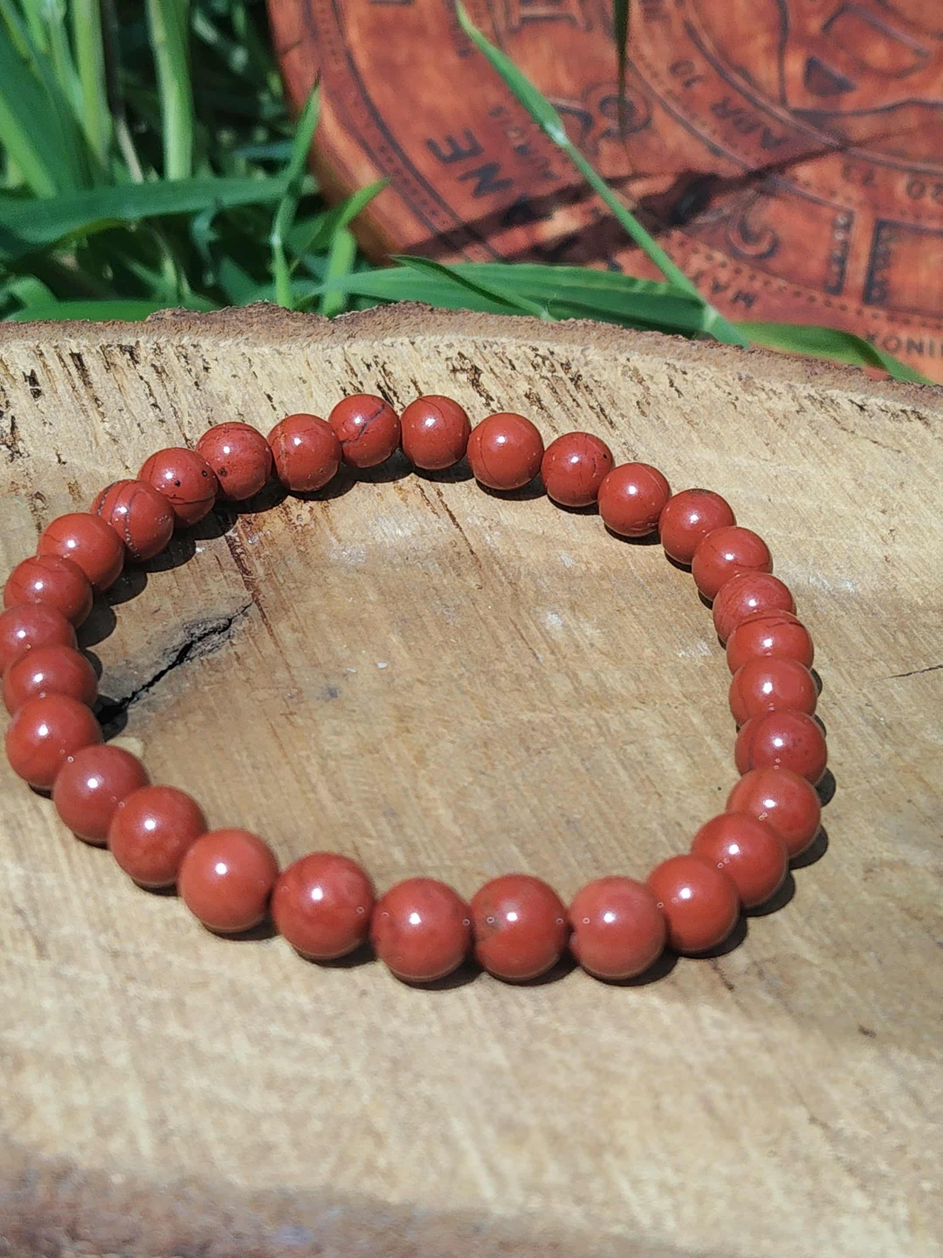 Bracelet jaspe rouge 6 mm sur tranche de bois avec herbes vertes et décor ésotérique, perles rouge brique pour courage posé, ancrage et présence solide