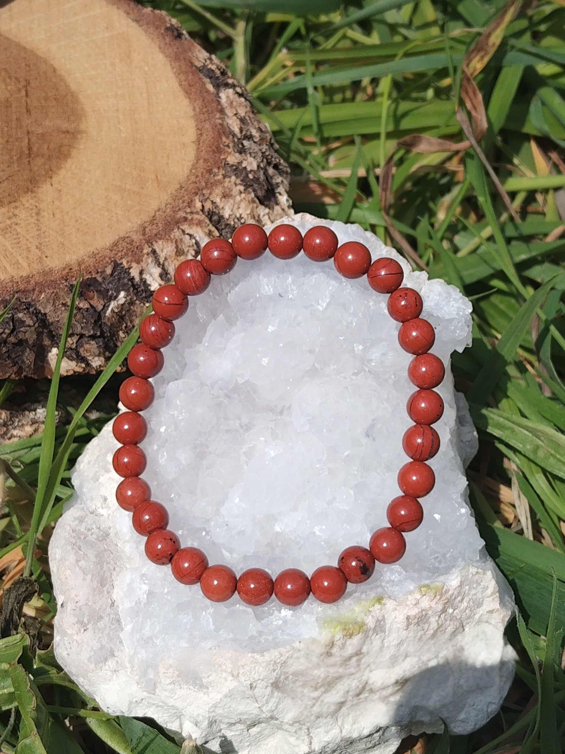 Bracelet jaspe rouge 6 mm posé sur amas de quartz blanc et bois brut, perles rouge profond, élan vital, courage et présence