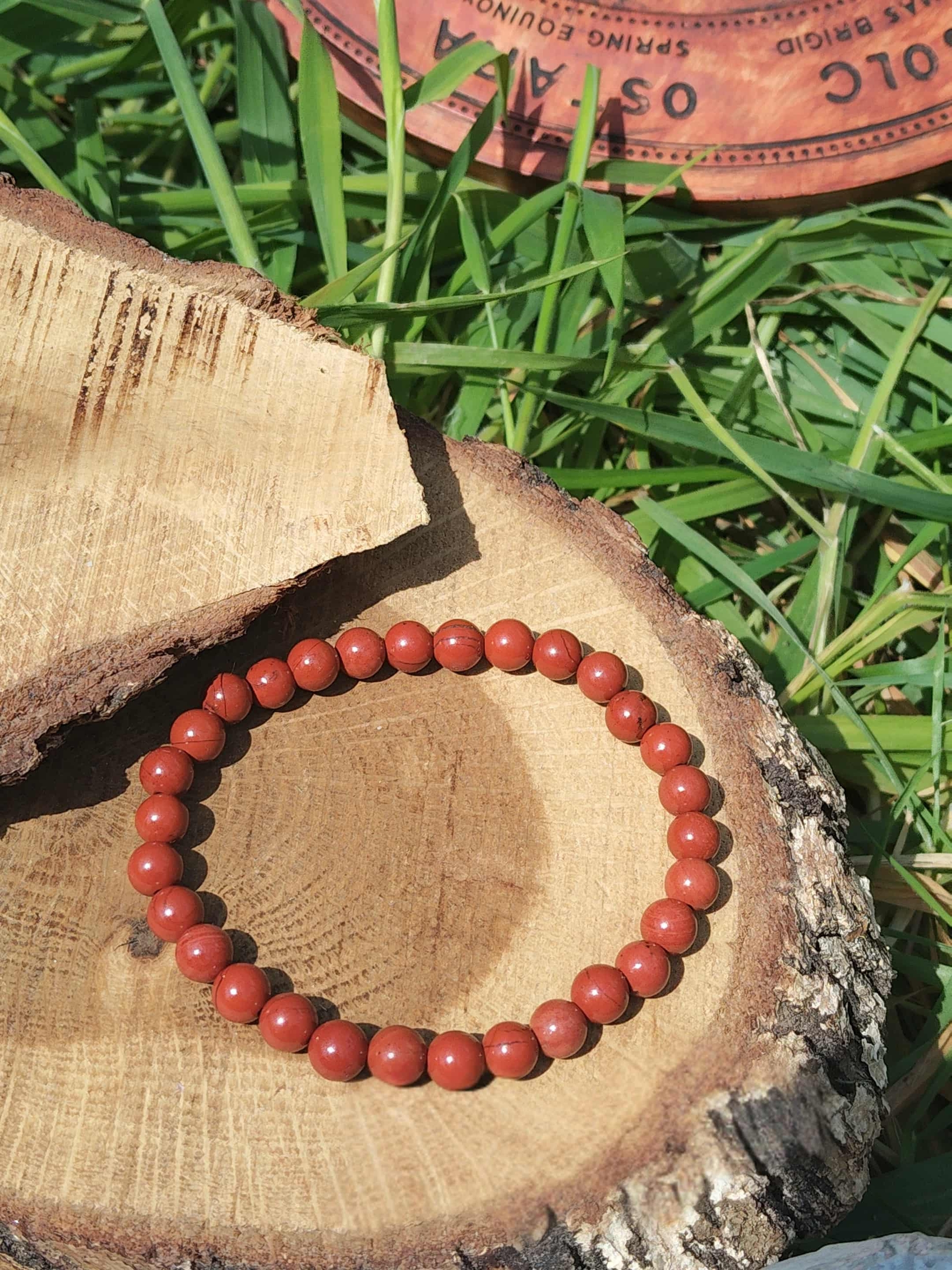 Bracelet jaspe rouge 6 mm sur rondelle de bois dans l’herbe, perles rouge ocre pour persévérance, constance et passage à l’action