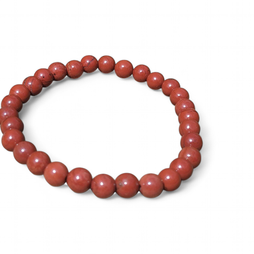 Bracelet jaspe rouge 6 mm posé sur amas de quartz blanc et bois brut, perles rouge profond pour volonté, feu intérieur et tenue émotionnelle