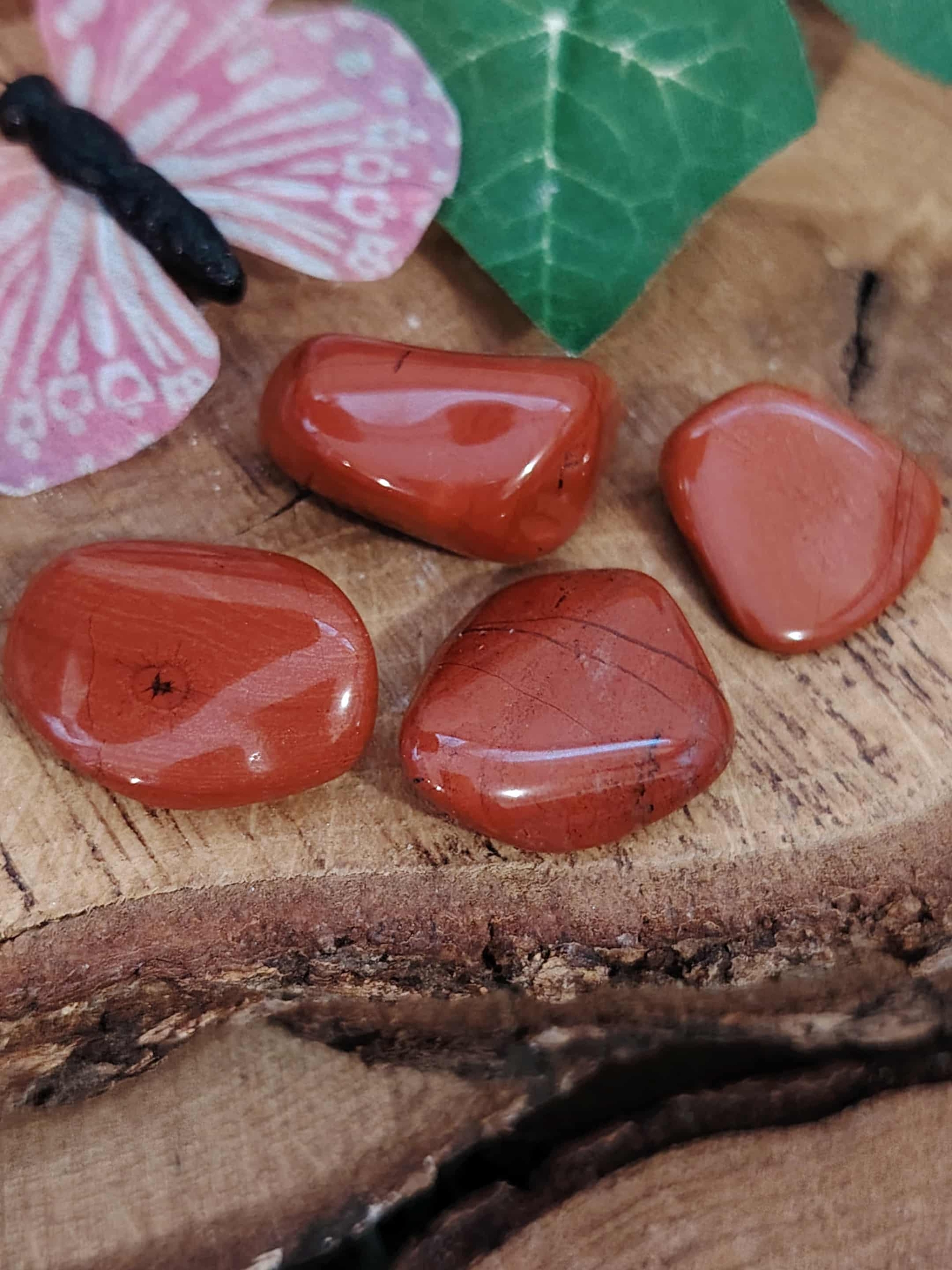 Pierres naturelles de jaspe rouge sur rondin de bois, pierres roulées associées à la sécurité intérieure, à l’enracinement et à la confiance calme.