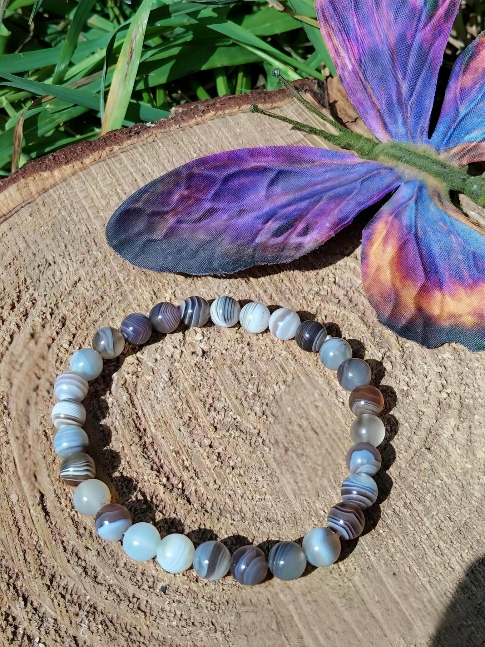Bracelet Agate du Botswana sur tranche de bois avec papillon multicolore, ancrage rassurant et protection apaisante