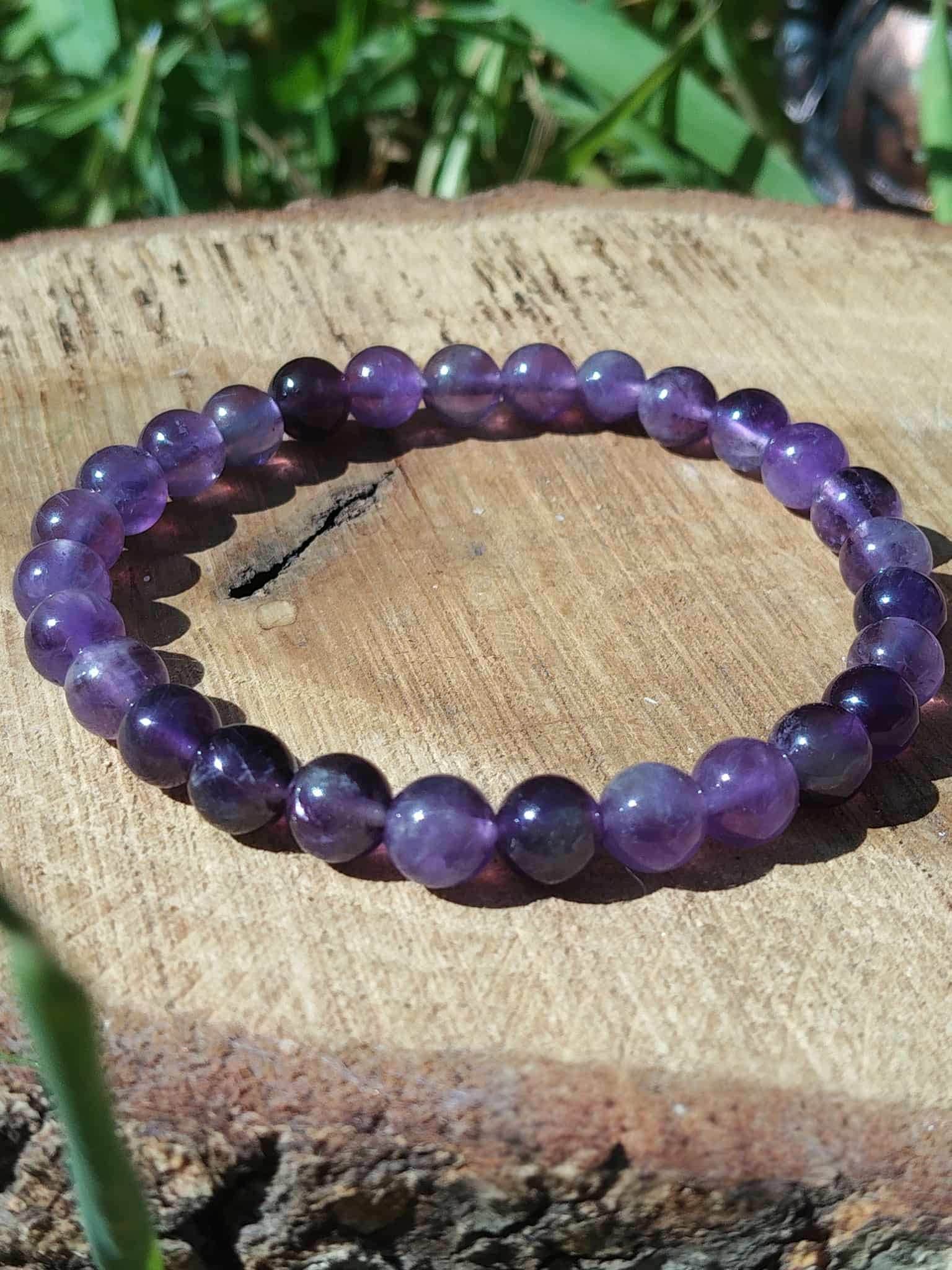 Bracelet en améthyste posé sur bois avec fond végétal, nuances violettes naturelles pour détente nerveuse, lucidité et recentrage