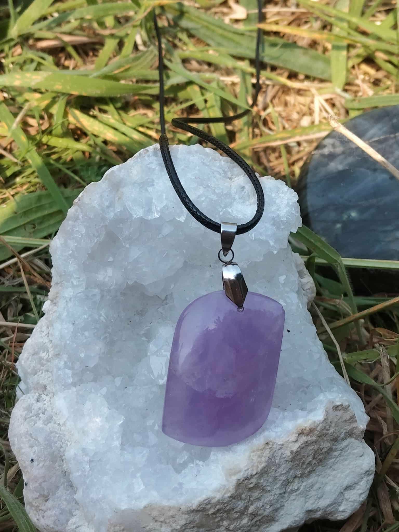 Pendentif améthyste violette posé sur amas de cristal et herbe, paix intérieure et élévation douce