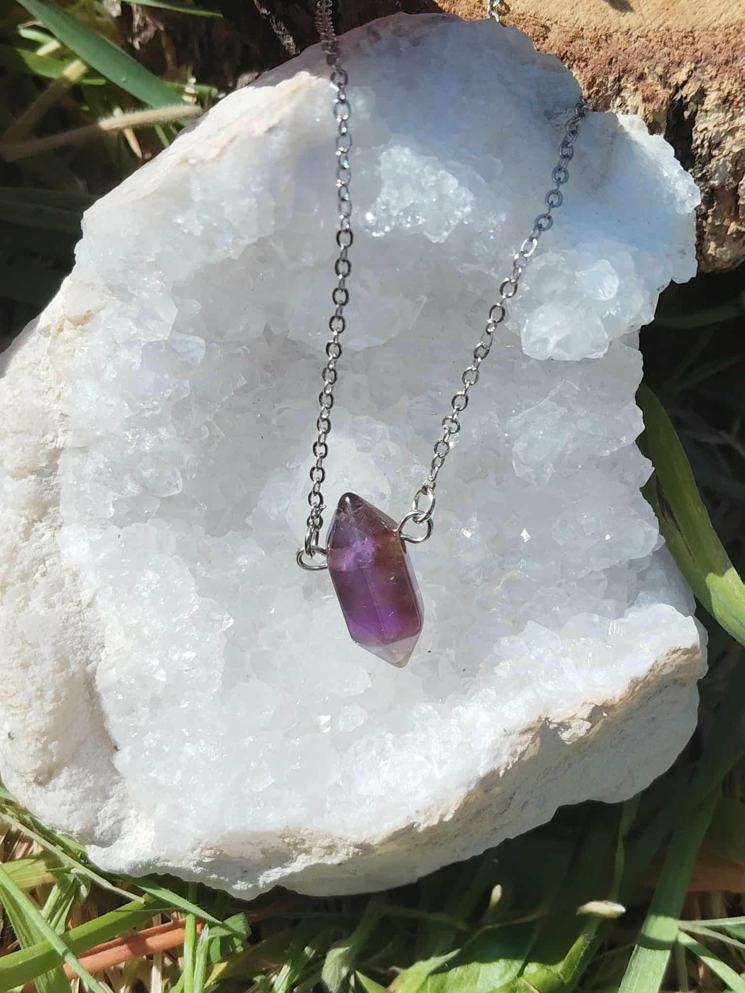 Collier pendentif pointe d’améthyste violette posé sur géode blanche, pierre naturelle reliée au calme des pensées, à la protection énergétique et à la paix intérieure.