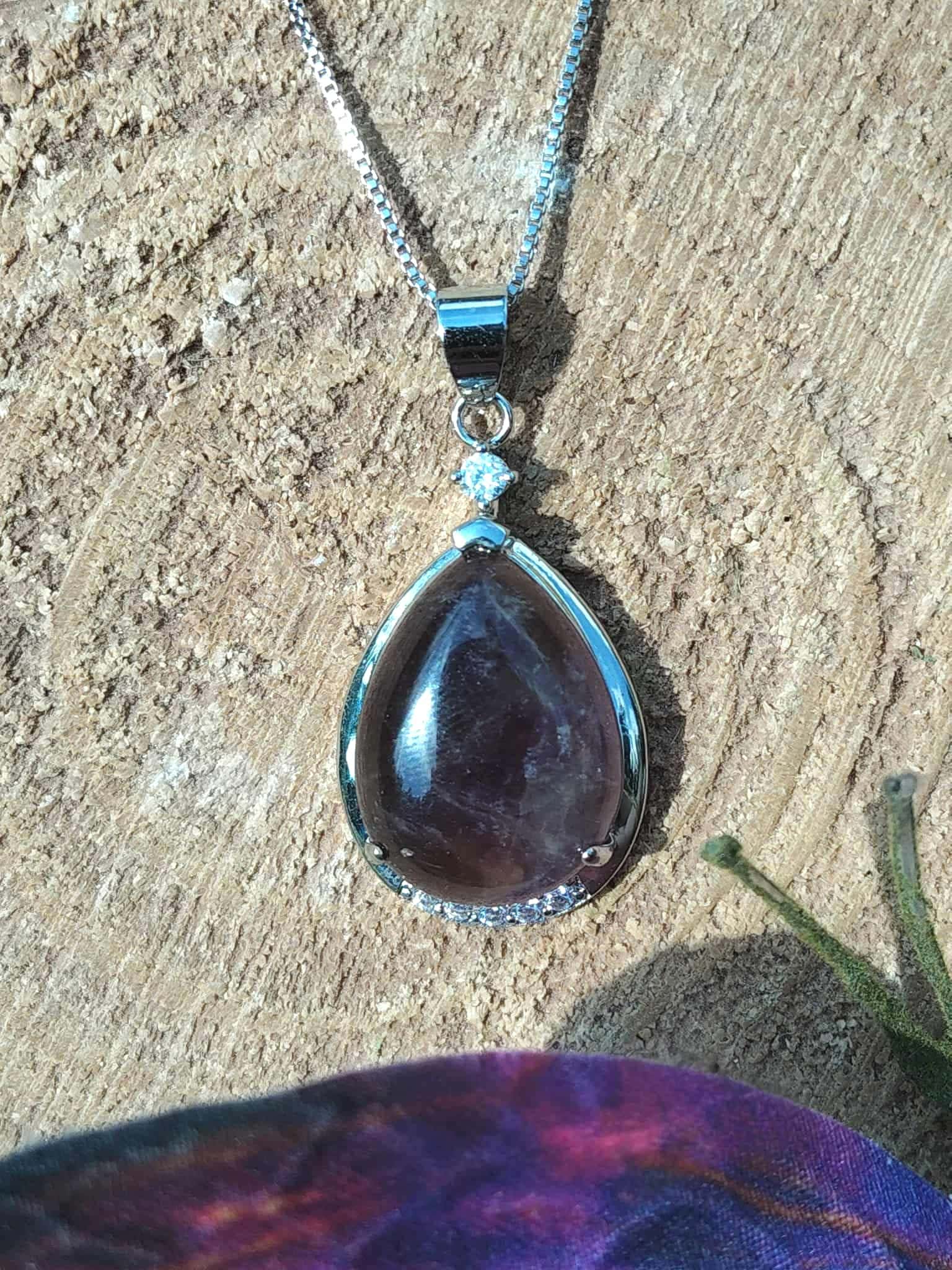 Pendentif goutte améthyste posé sur rondin de bois avec décor féerique, apaisement émotionnel et intuition tranquille