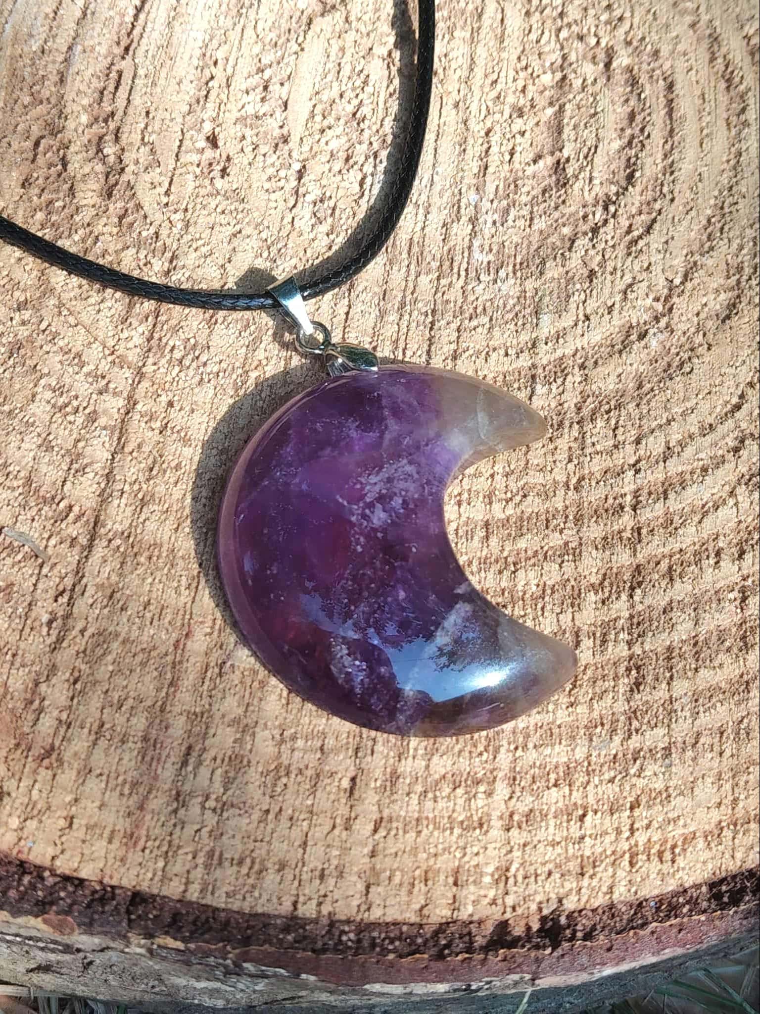 Pendentif lune en améthyste suspendu sur cordon noir, posé sur bois naturel, collier pierre violette inspirant détente, équilibre du cœur et sensibilité intuitive.