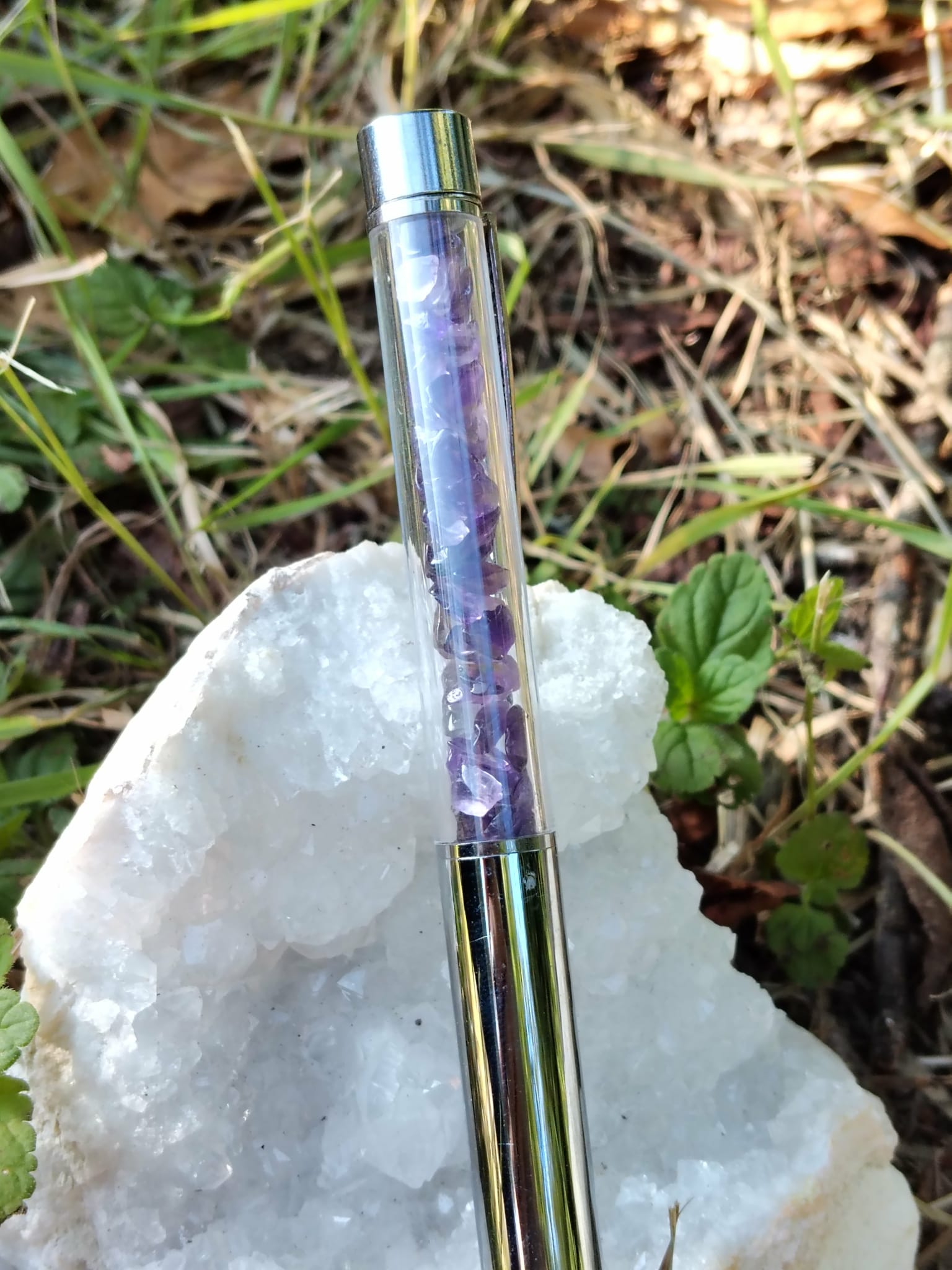 Stylo bille améthyste posé sur une géode de cristal dans l’herbe, accessoire d’écriture en pierres naturelles pour créativité, concentration et sérénité – boutique Magic Gaïa.