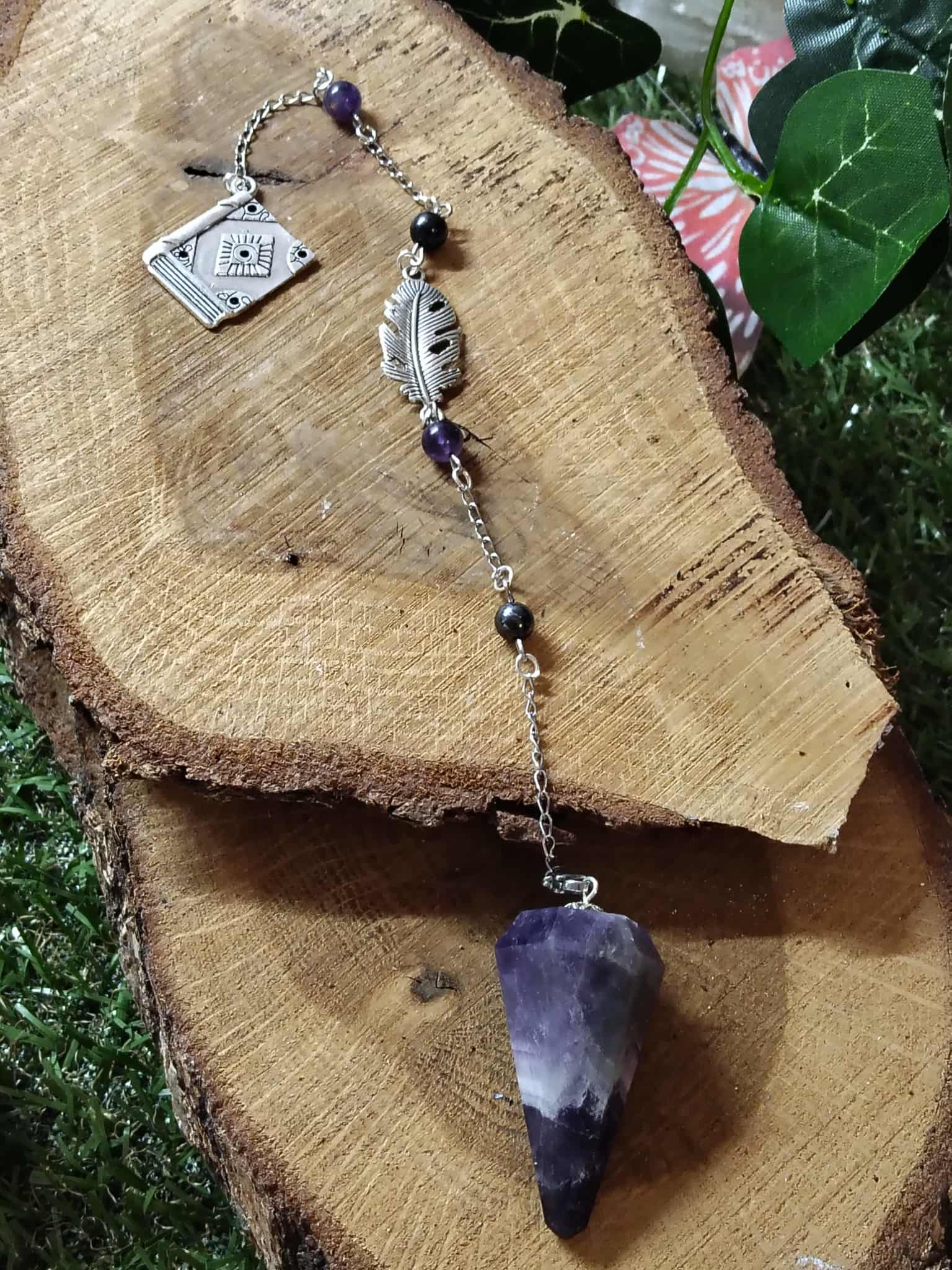 Pendule personnalisé en améthyste naturelle avec chaîne argentée, perles et breloque carrée, outil de radiesthésie ésotérique posé sur tranches de bois en décor nature.