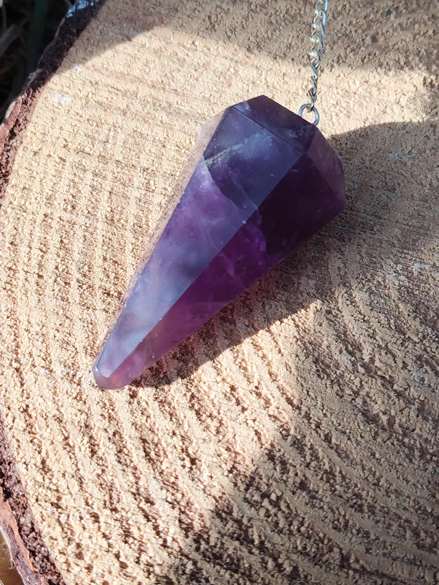 Pendule améthyste en pierre naturelle pour radiesthésie, intuition et spiritualité, posé sur chapeau de paille, outil énergétique pour apaisement mental et bien-être émotionnel.