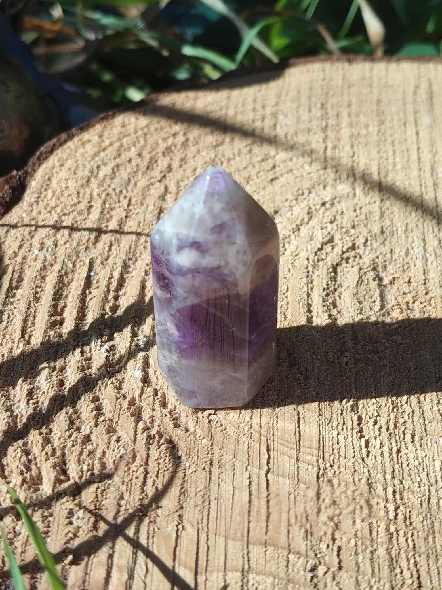 Petite pointe d’améthyste violette photographiée en extérieur sur support bois, cristal naturel lié à la finesse intuitive, au calme et à la sérénité.
