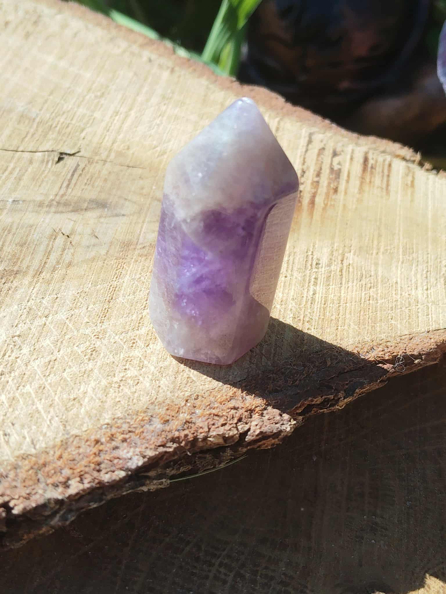 Pointe d’améthyste en pierre naturelle posée sur tranche de bois en extérieur, cristal violet évoquant la douceur du cœur, la lucidité et la paix intérieure.
