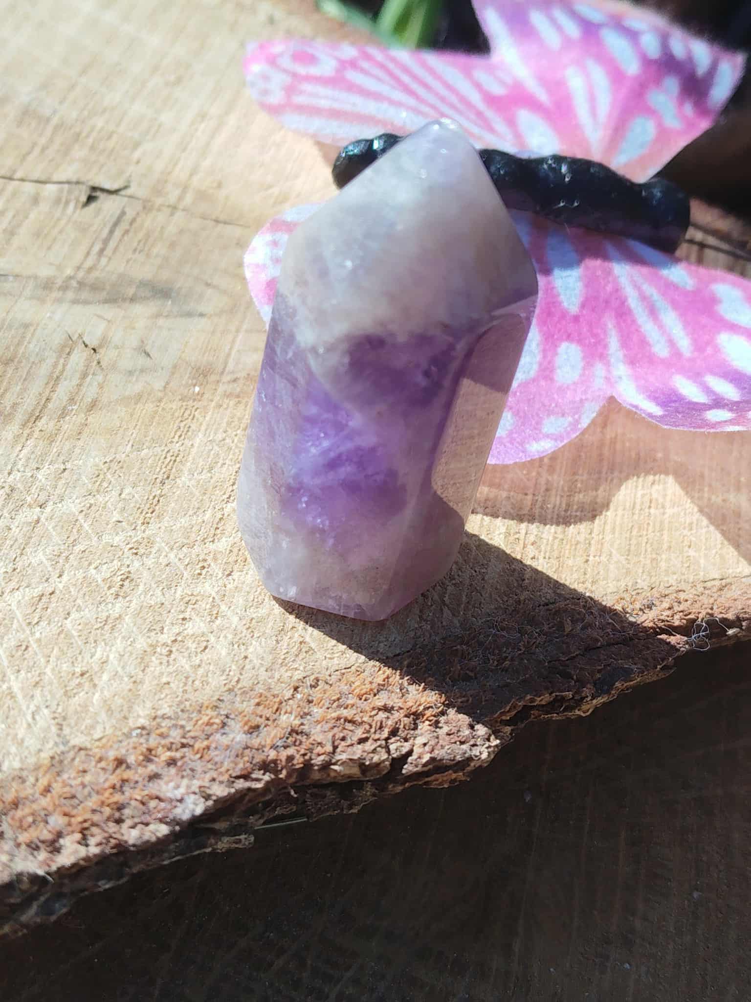 Pointe d’améthyste naturelle posée sur tranche de bois avec décoration papillon, cristal violet associé à la sérénité, à l’intuition et à la douceur intérieure.