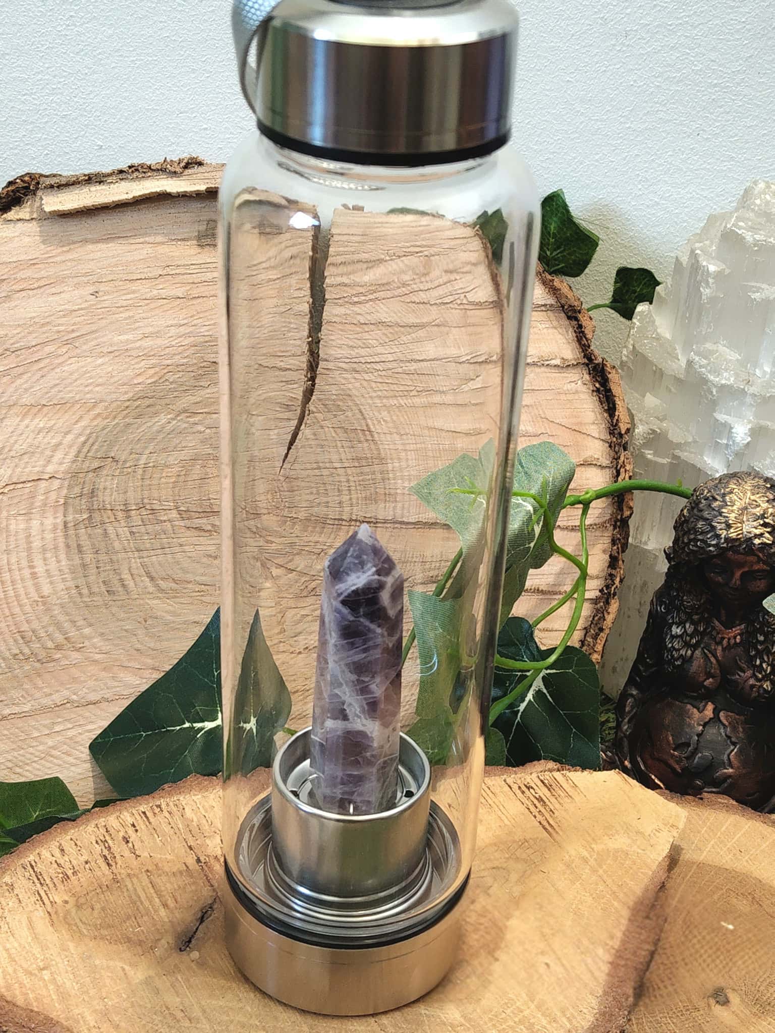 Bouteille d’eau en verre améthyste, 500 ml, sur rondin de bois décoratif, objet de lithothérapie pour allier hydratation, énergie et apaisement.