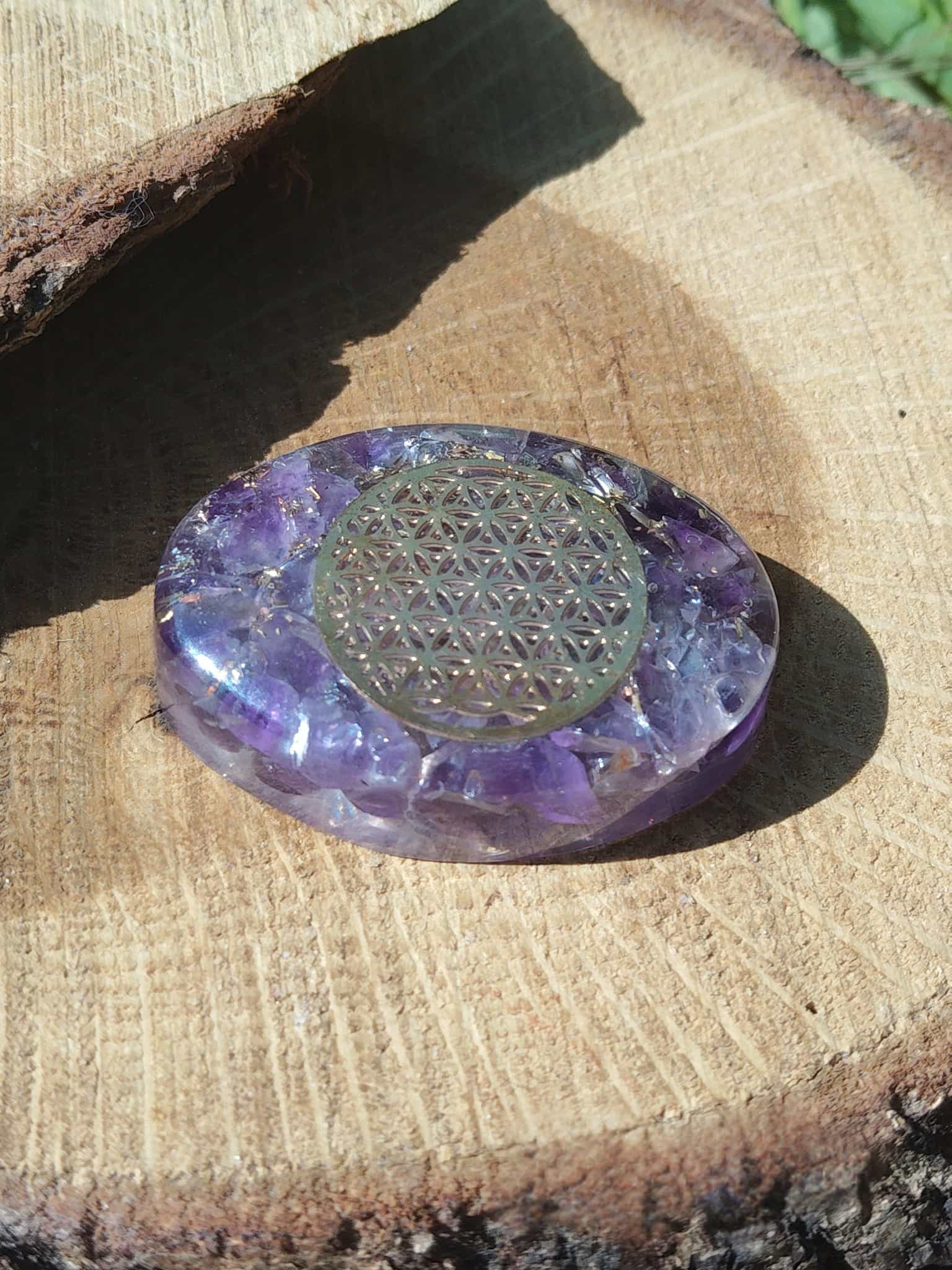 Petit galet énergétique en orgonite améthyste décoré d’une fleur de vie, présenté sur support en bois naturel, idéal pour apaiser l’ambiance, équilibrer les énergies et soutenir le bien-être spirituel