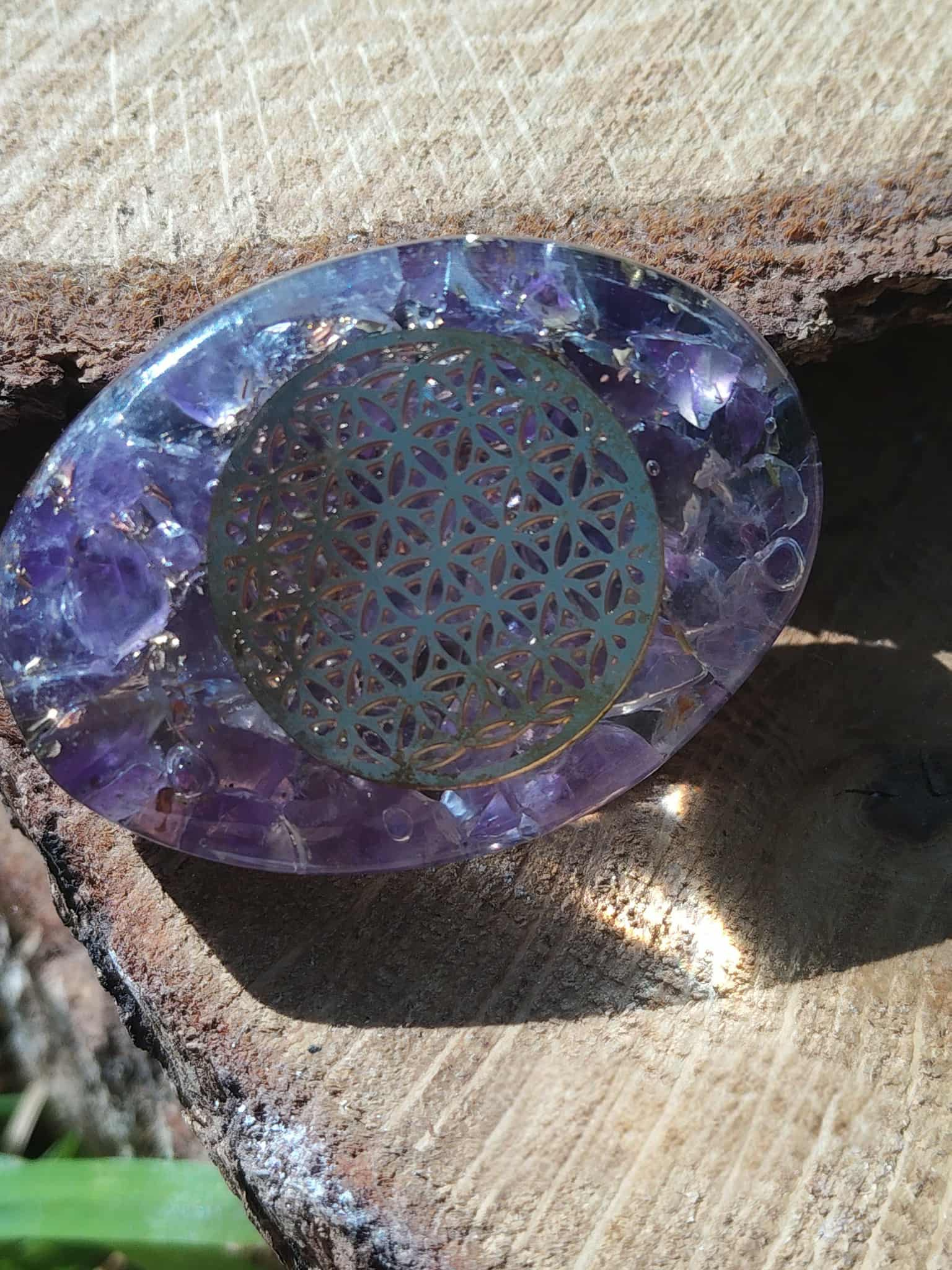 Galet orgonite améthyste aux reflets bleus avec fleur de vie centrale, photographié sur bois, accessoire spirituel pour créer un coin zen et énergétique à la maison