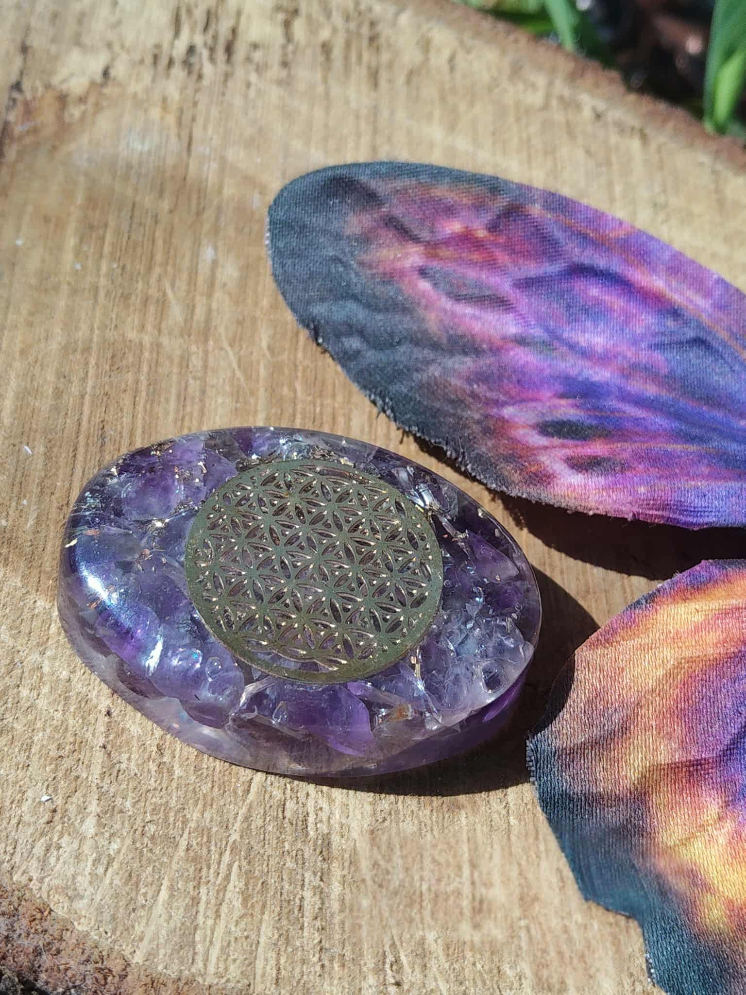 Galet en orgonite améthyste orné d’une fleur de vie, mis en scène sur bois avec papillon coloré, déco ésotérique pour coin rituel, énergie douce et vibration positive