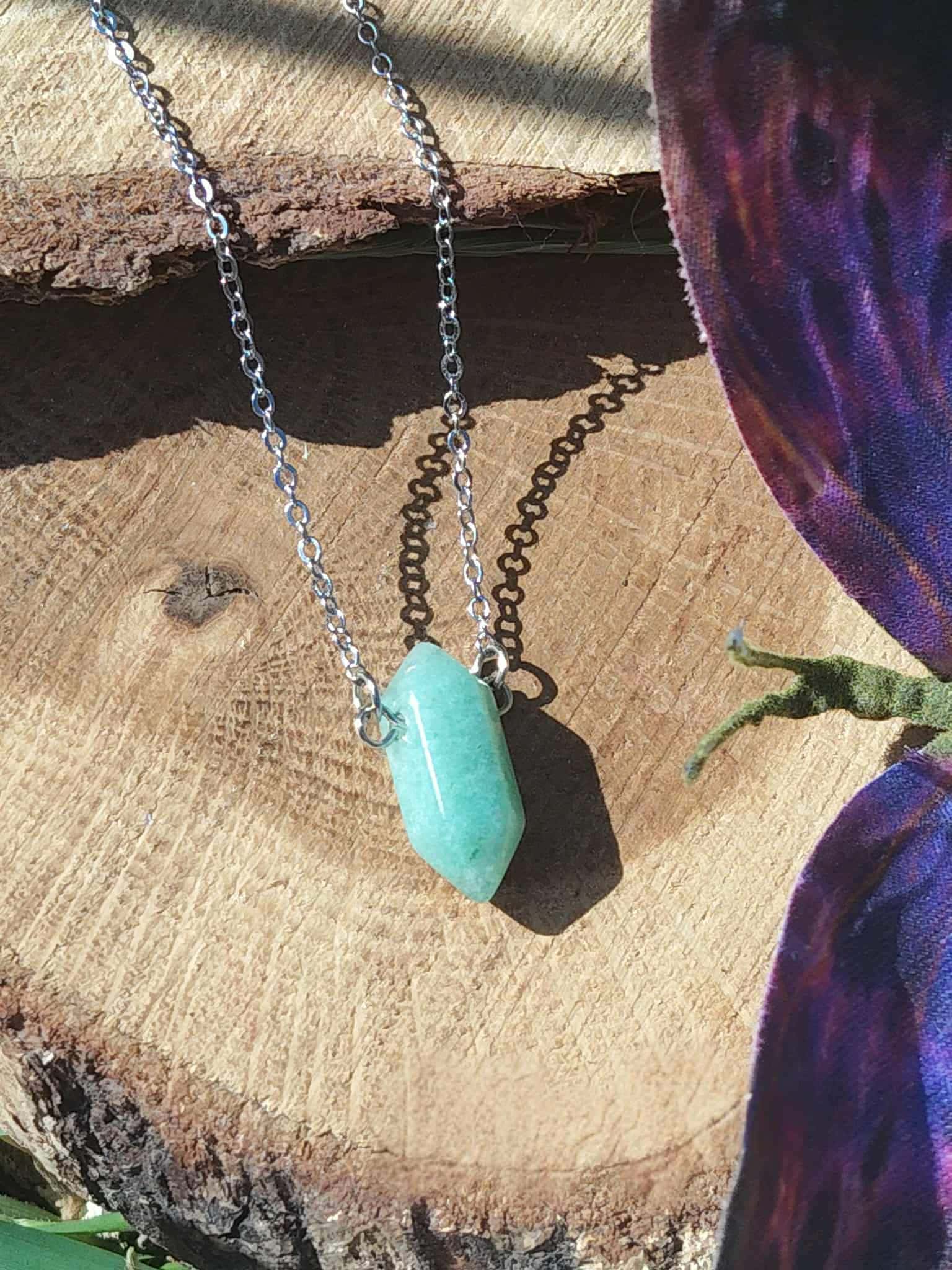 Pendentif pointe en aventurine verte sur chaîne argentée, posé sur tranche de bois avec décor naturel, bijou en pierre naturelle associé à l’apaisement, à l’équilibre émotionnel et à la douceur du cœur.