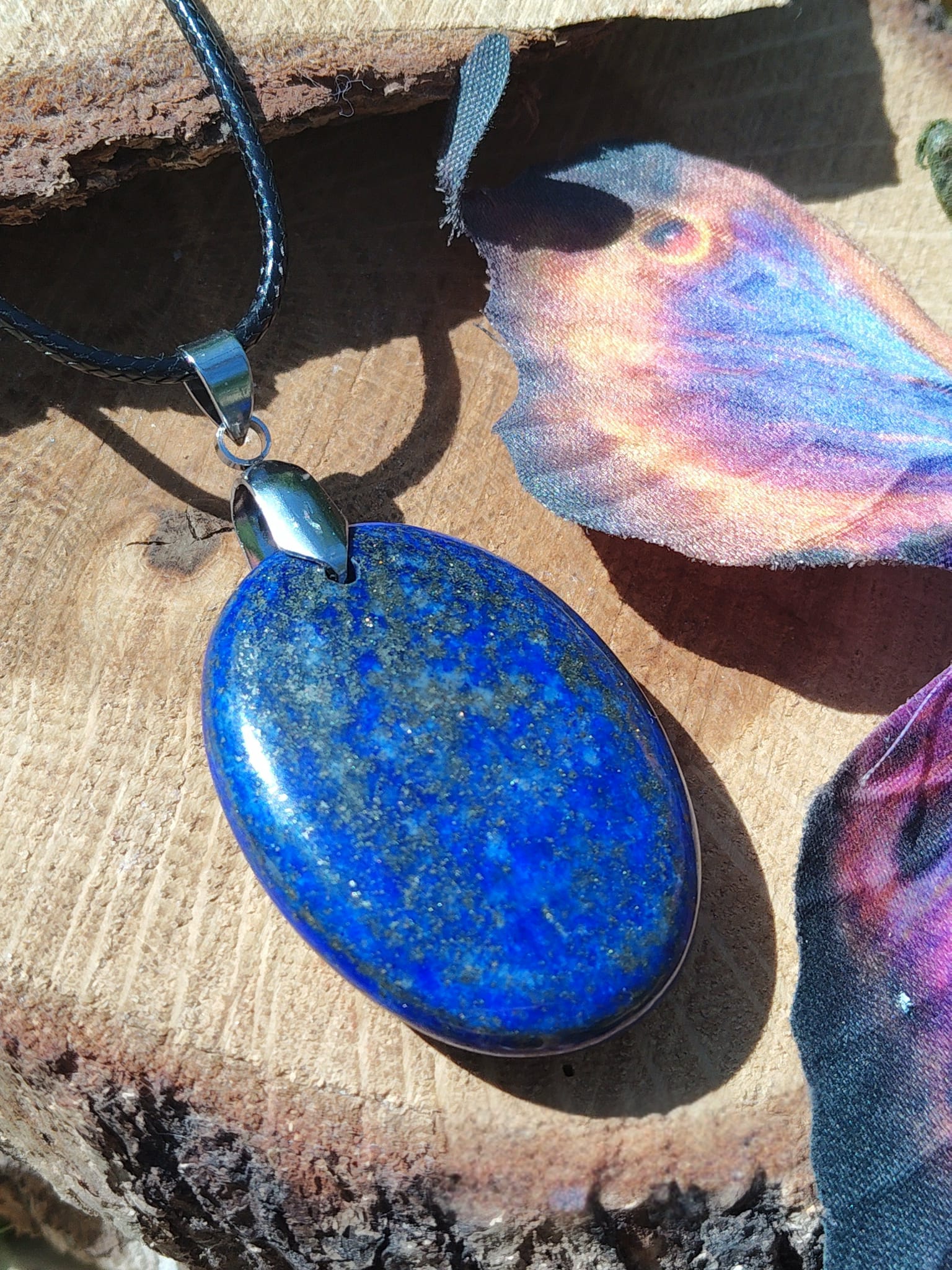 Pendentif en lapis lazuli bleu profond sur cordon noir posé sur fond bois, bijou en pierre naturelle associé à la clarté d’expression, à la sagesse et à l’équilibre émotionnel.