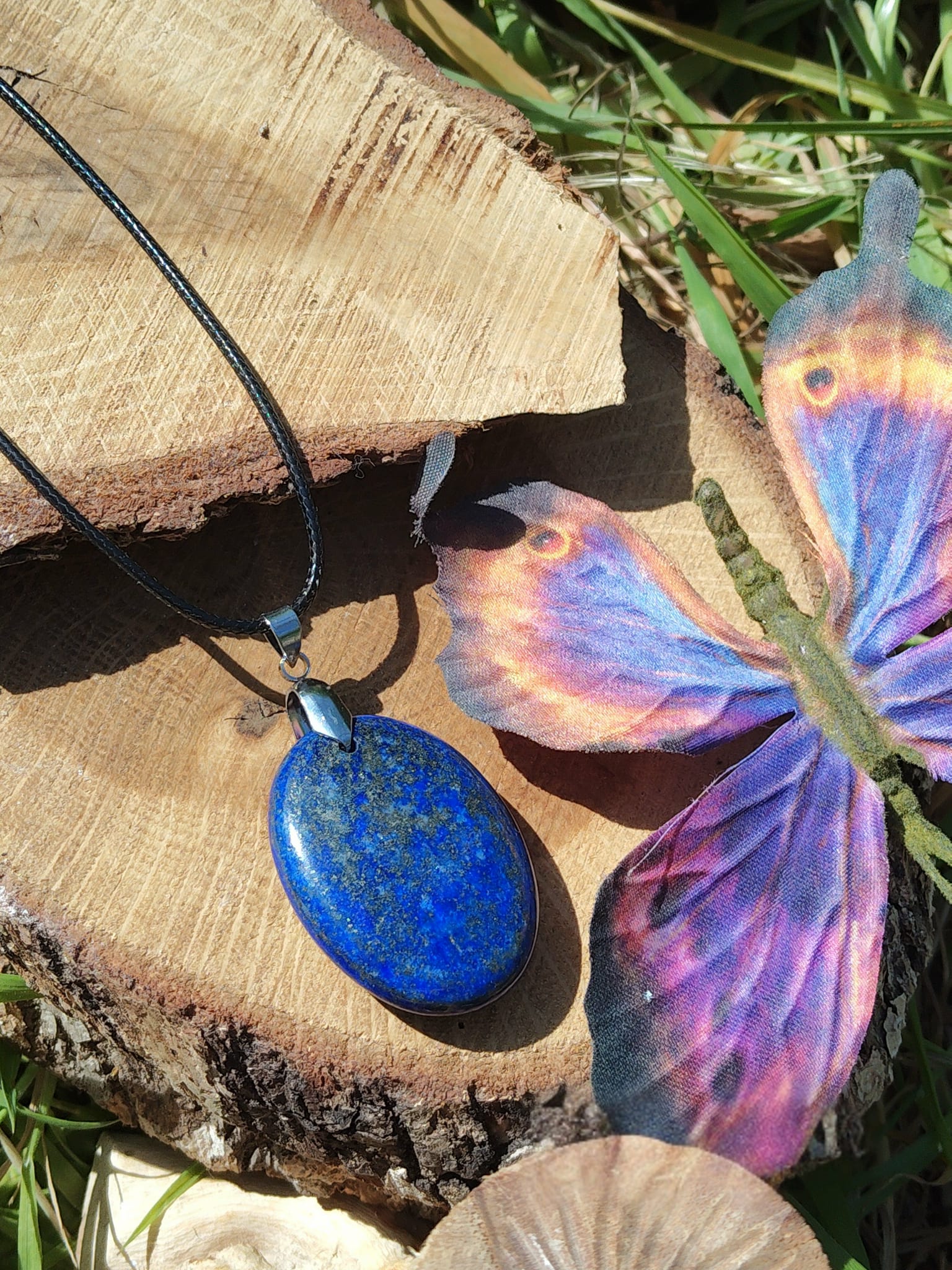 Pendentif lapis lazuli bleu sur support en bois avec papillon coloré, bijou naturel lié à l’inspiration, à l’aisance relationnelle et au calme du mental.