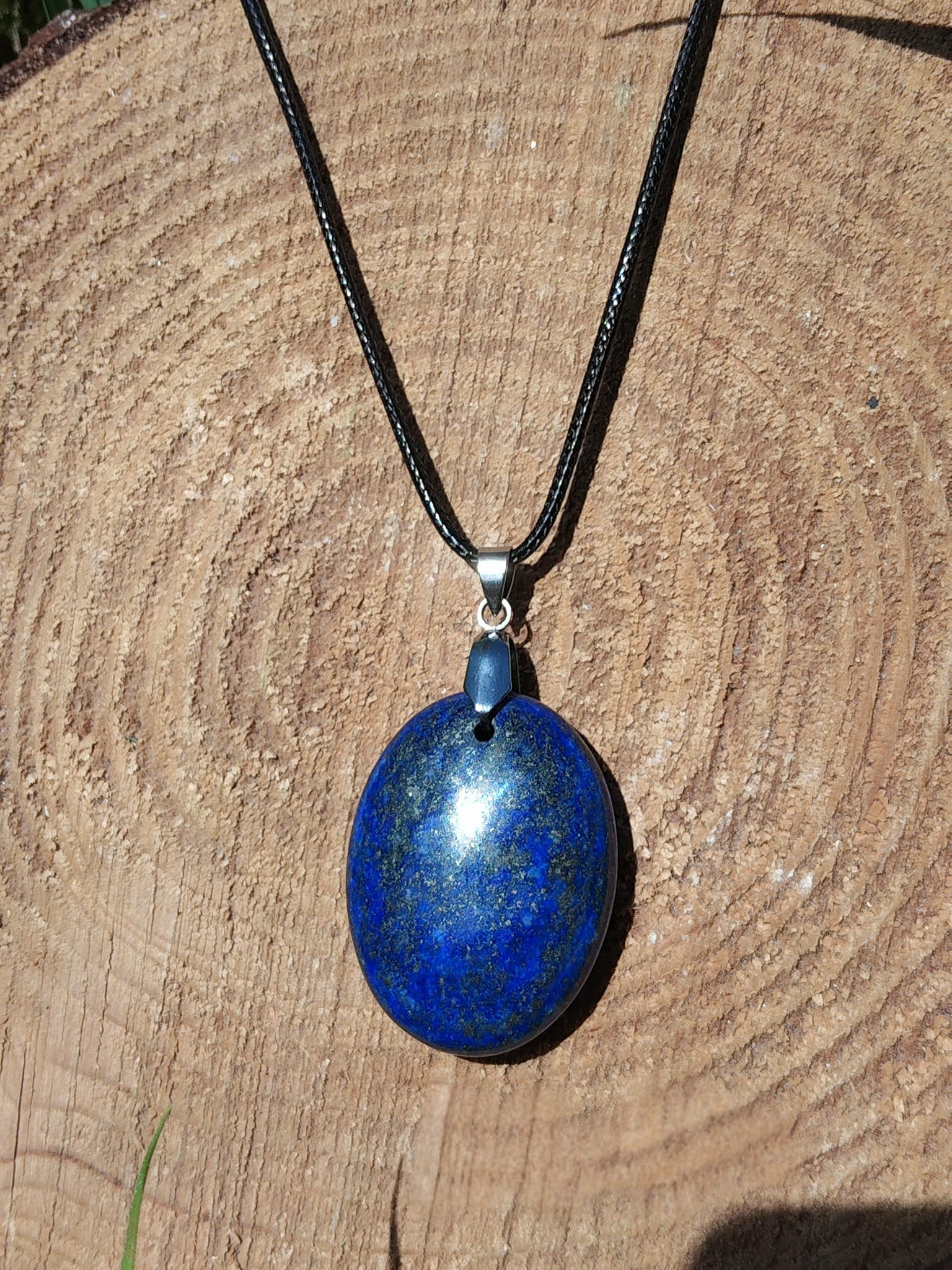 Pendentif lapis lazuli bleu sur fond bois, pierre naturelle reliée à la maîtrise de soi, à l’apaisement des pensées et à l’intuition profonde.