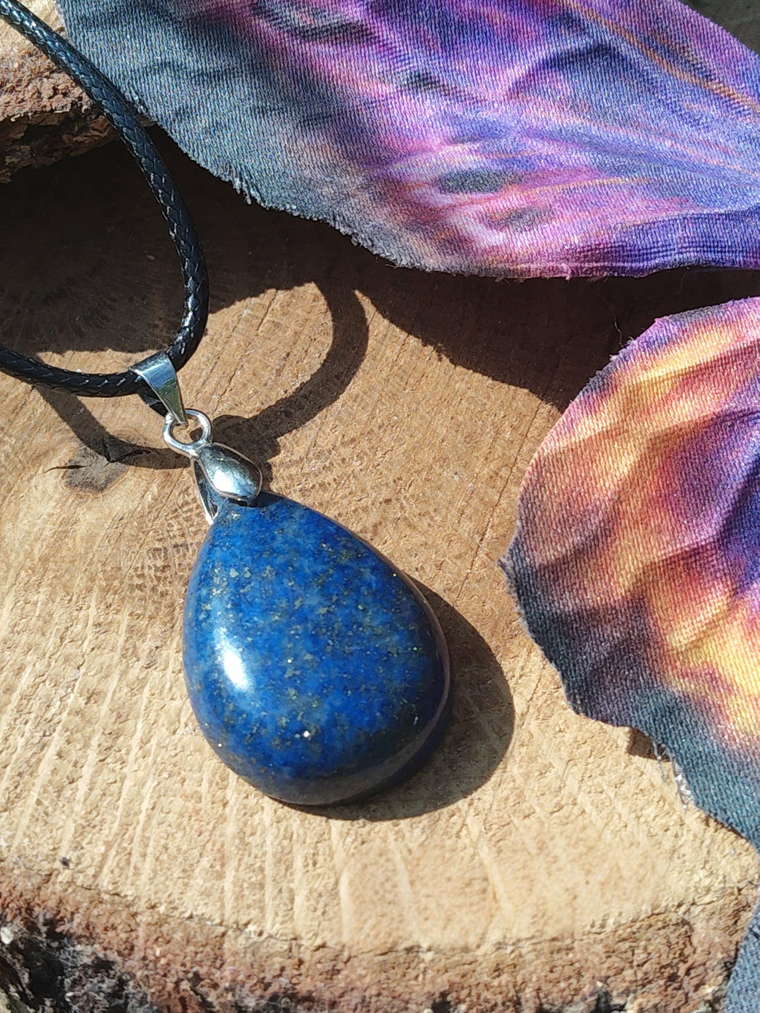 Pendentif goutte en lapis lazuli bleu sur rondin de bois avec ailes colorées, collier en pierre naturelle associé à la lucidité, à l’écoute intérieure et à la sérénité.