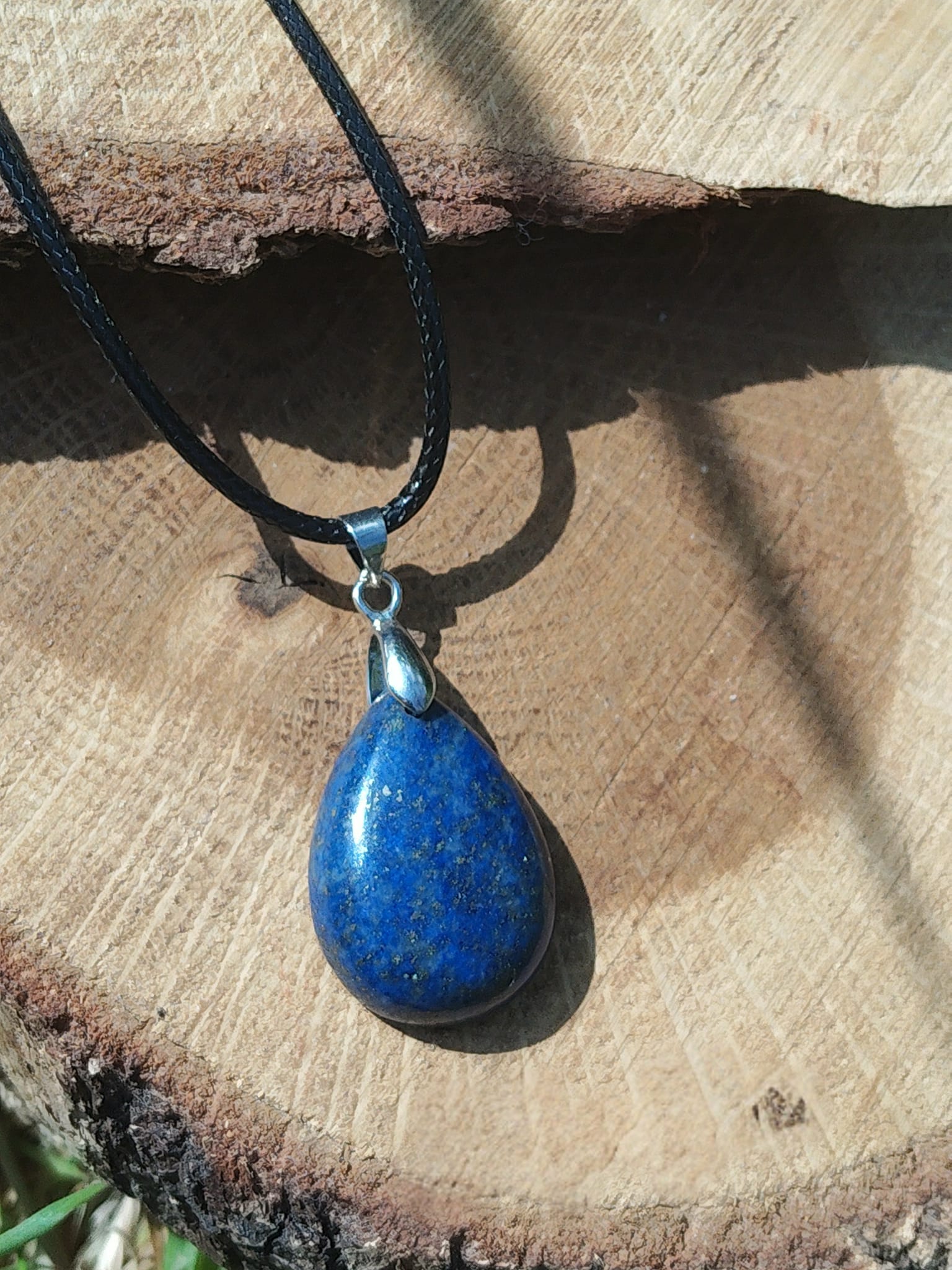 Pendentif goutte en lapis lazuli bleu sur rondin de bois, bijou Magic Gaïa en pierre naturelle associé à la maîtrise de soi, à la clarté mentale et à l’équilibre intérieur.