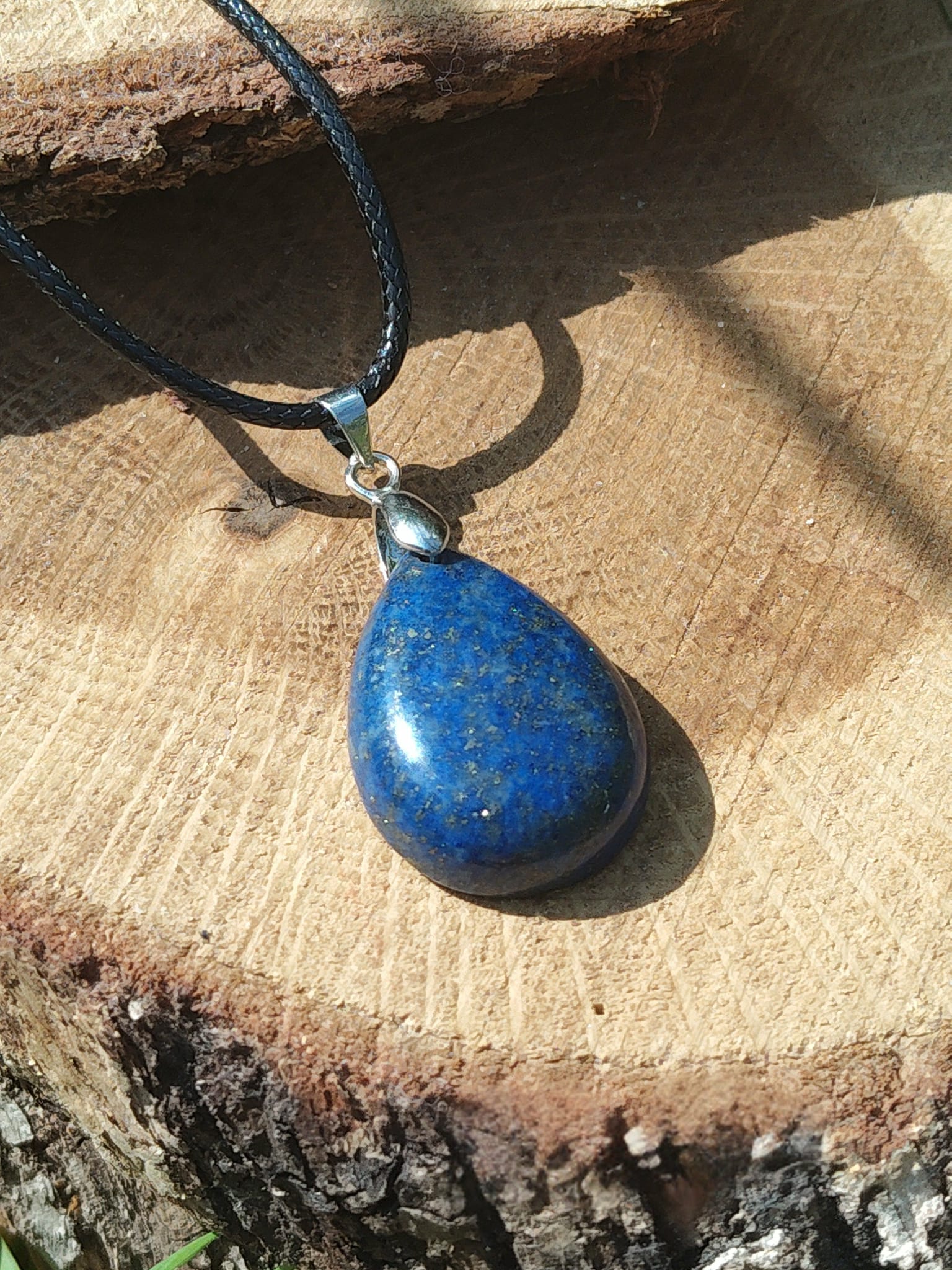 Pendentif goutte en lapis lazuli bleu posé sur rondin de bois, bijou lithothérapie évoquant la parole fluide, la présence d’esprit et le calme intérieur