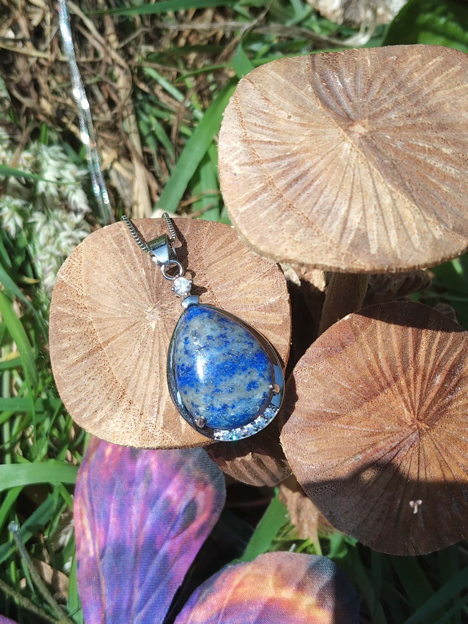 Pendentif goutte en lapis lazuli bleu posé sur champignons décoratifs en extérieur, bijou en pierre naturelle lié à l’intuition, au recentrage et à l’harmonie intérieure.