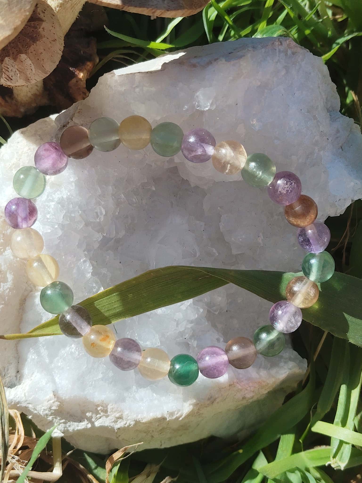 Bracelet fluorite multicolore sur grande pierre blanche en extérieur, perles colorées et lumineuses, vision claire et recentrage