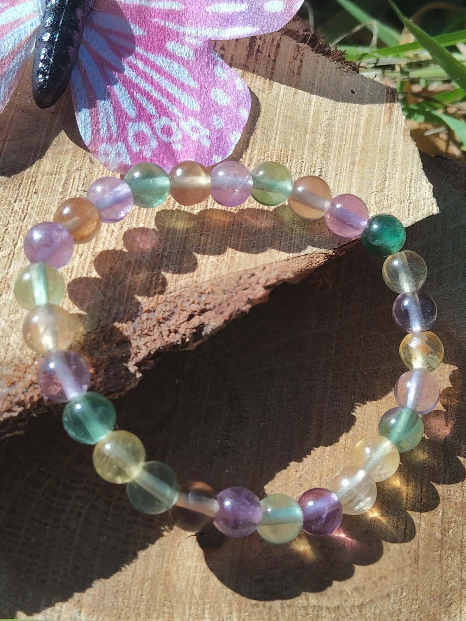 Bracelet fluorite multicolore sur tranche de bois en extérieur, perles naturelles aux nuances vertes et violettes, clarté d’esprit et recul émotionnel